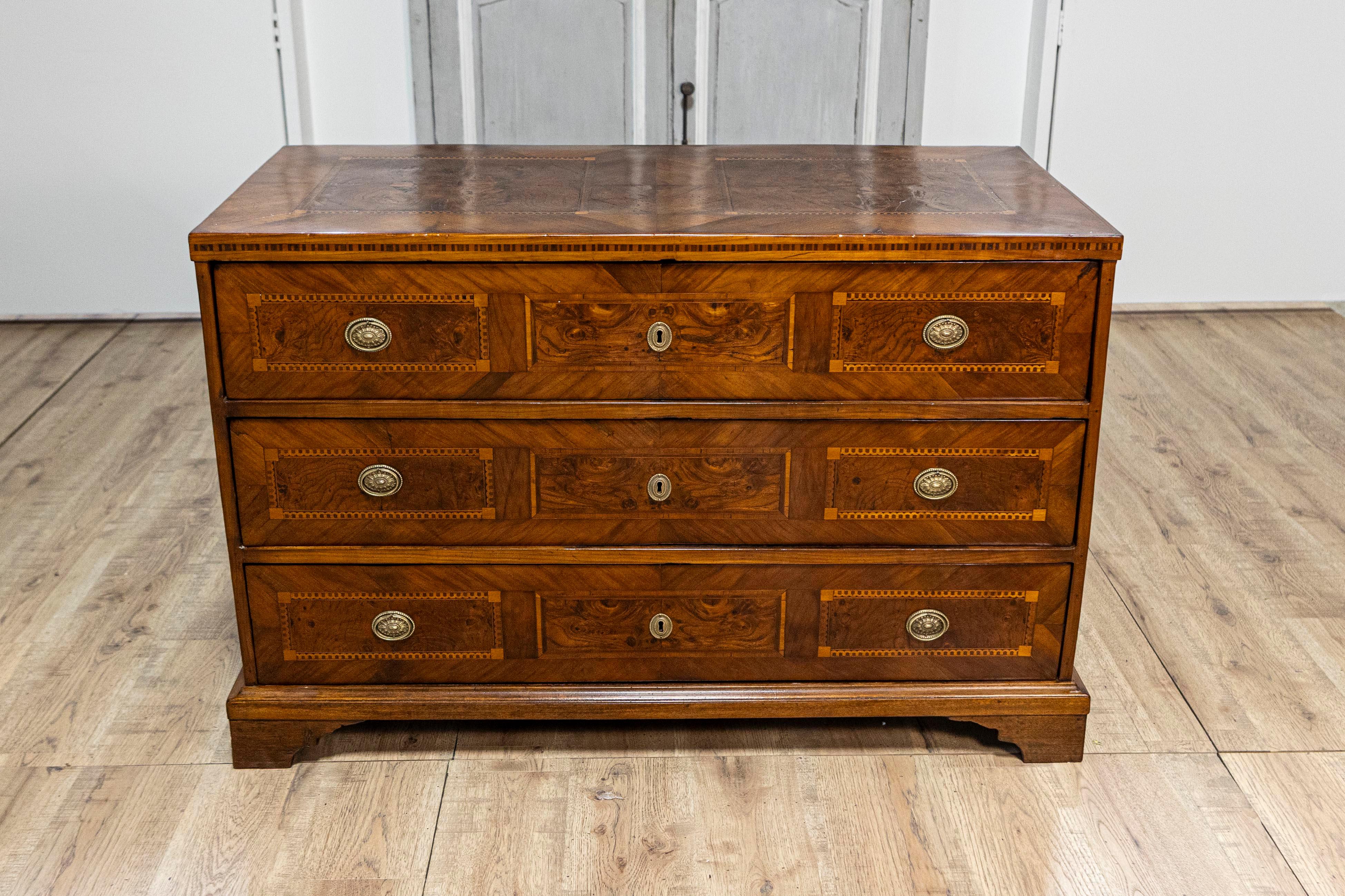 An Italian walnut and mahogany commode from the 19th century with three drawers, inlay and bracket feet. This 19th-century Italian commode beautifully exemplifies classic craftsmanship with its rich walnut and mahogany construction. The commode