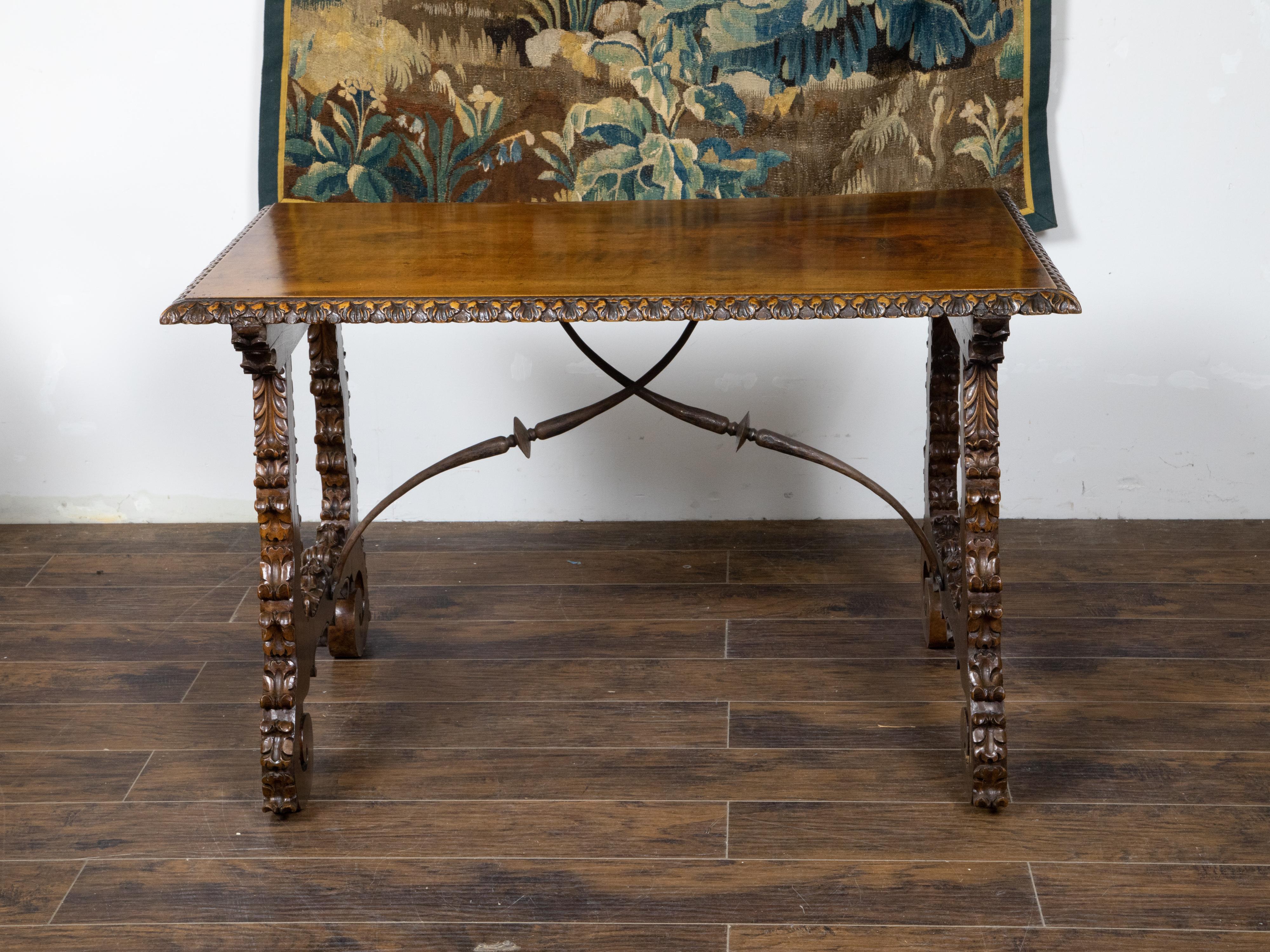 An Italian Baroque style walnut Fratino console table from the 19th century, with carved lyre-shaped trestle base, scrolling foliage motifs, iron stretchers, carved feet and brown patina. Created in Italy during the 19th century, this Baroque walnut