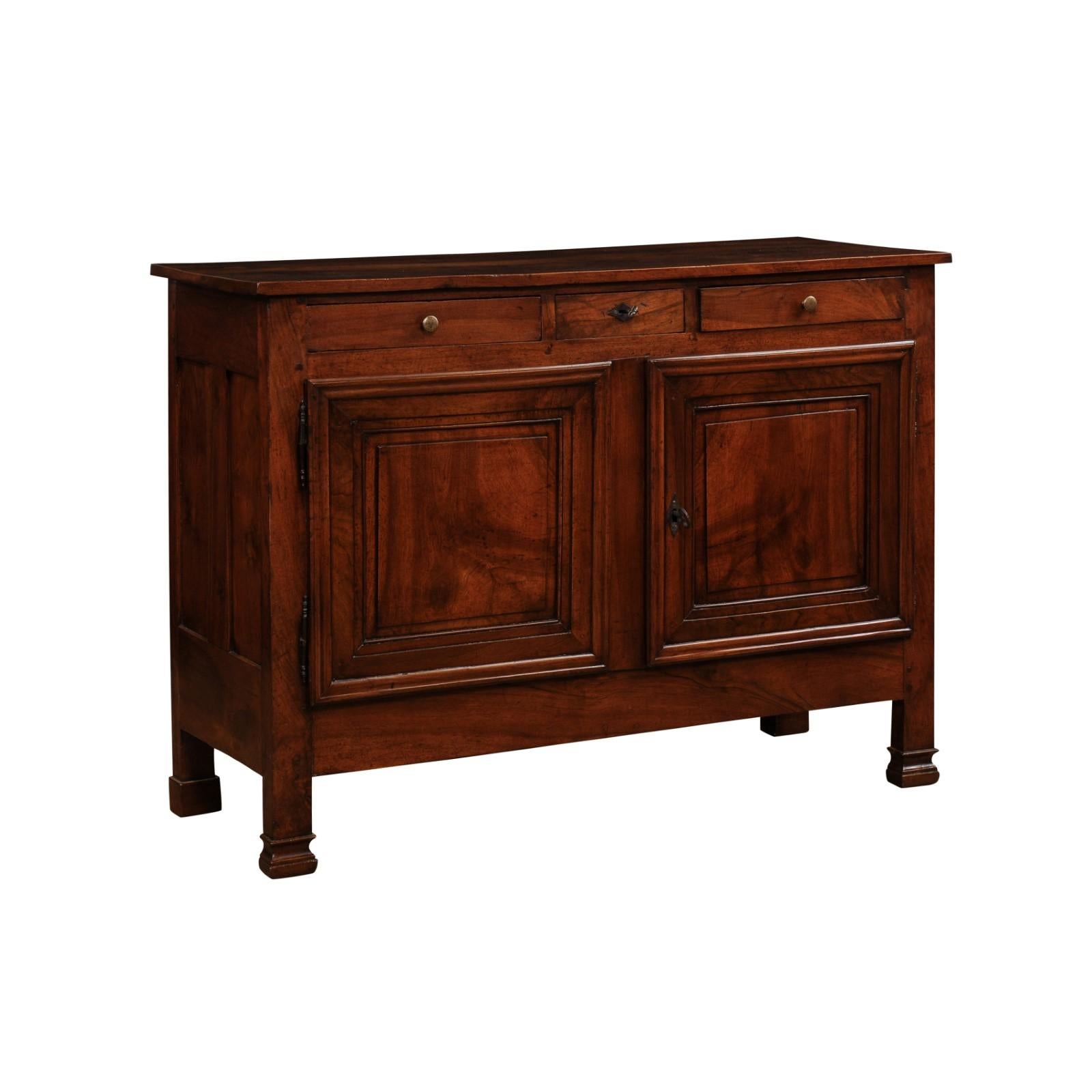 An Italian walnut buffet from the 19th century, with three drawers, a pair of molded doors and delicately carved front feet. Created in Italy during the 19th century, this walnut buffet features a simple rectangular top sitting above two drawers