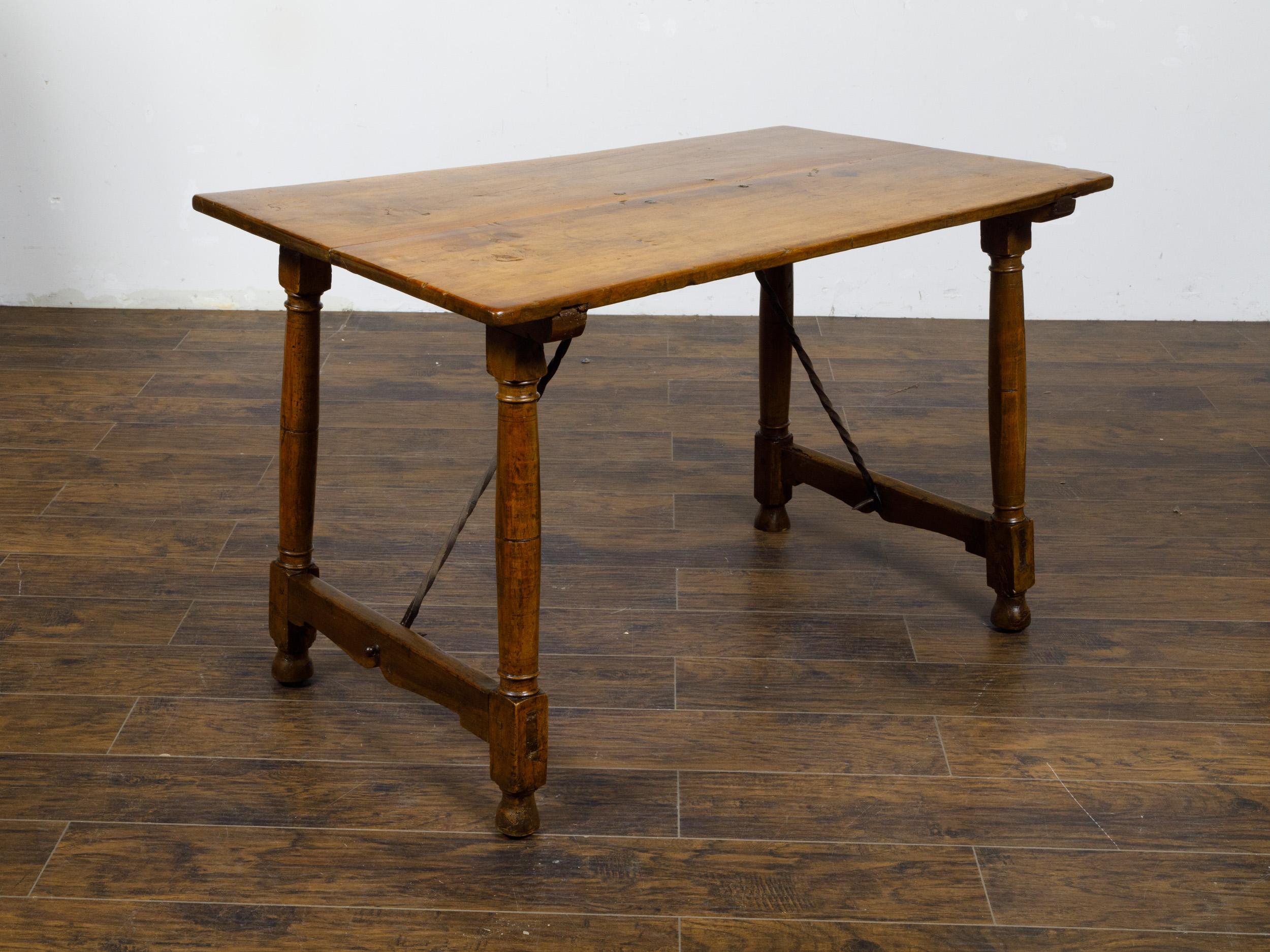 An Italian walnut console table from the 19th century with column shaped legs and iron stretchers. This Italian walnut console table from the 19th century stands as a testament to the timeless appeal of rustic elegance. With its slender, slightly