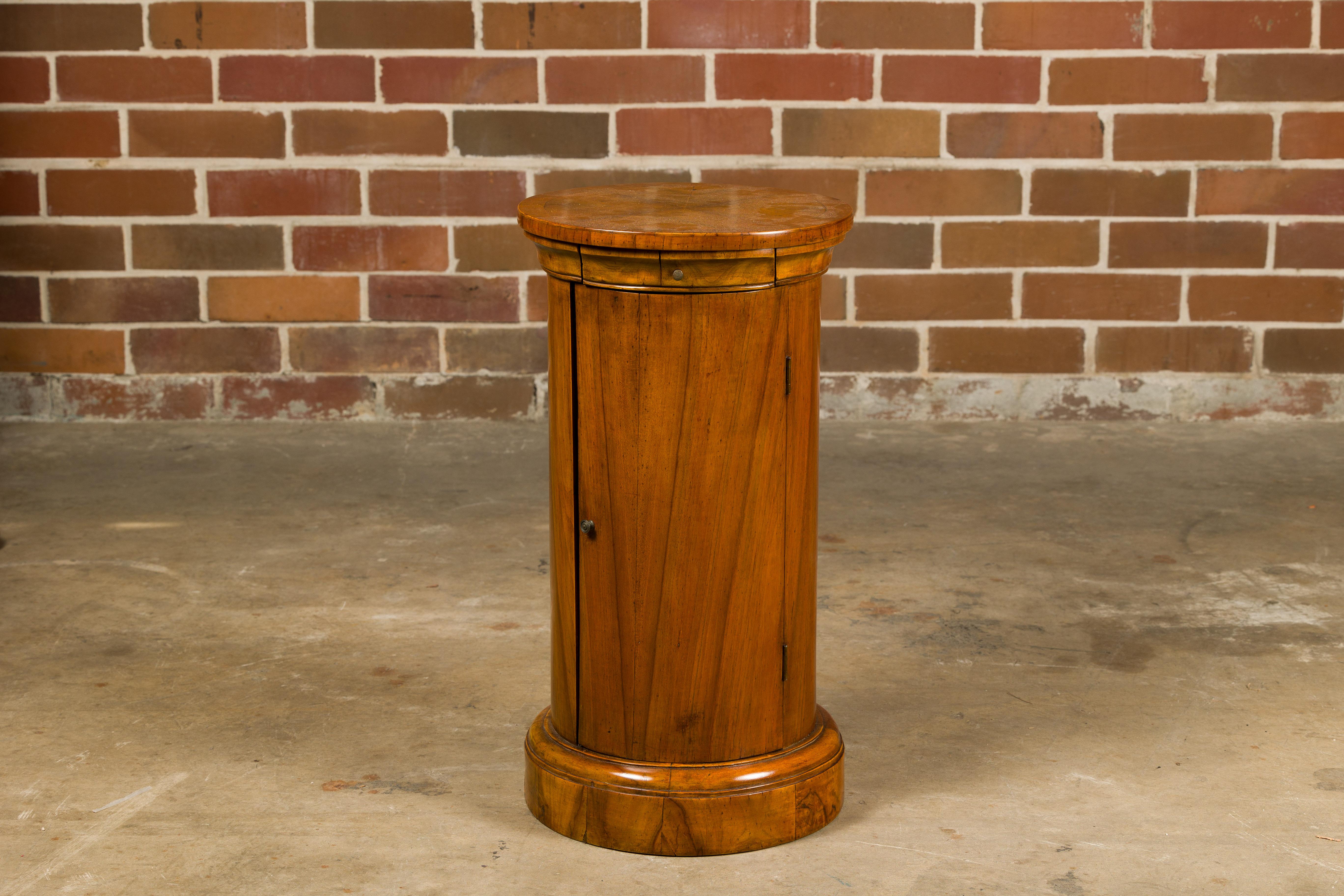An Italian walnut drum table from the 19th century with bookmatched top, single door and single drawer. This 19th-century Italian walnut drum table is a testament to timeless craftsmanship and classic design. The table's surface is adorned with a