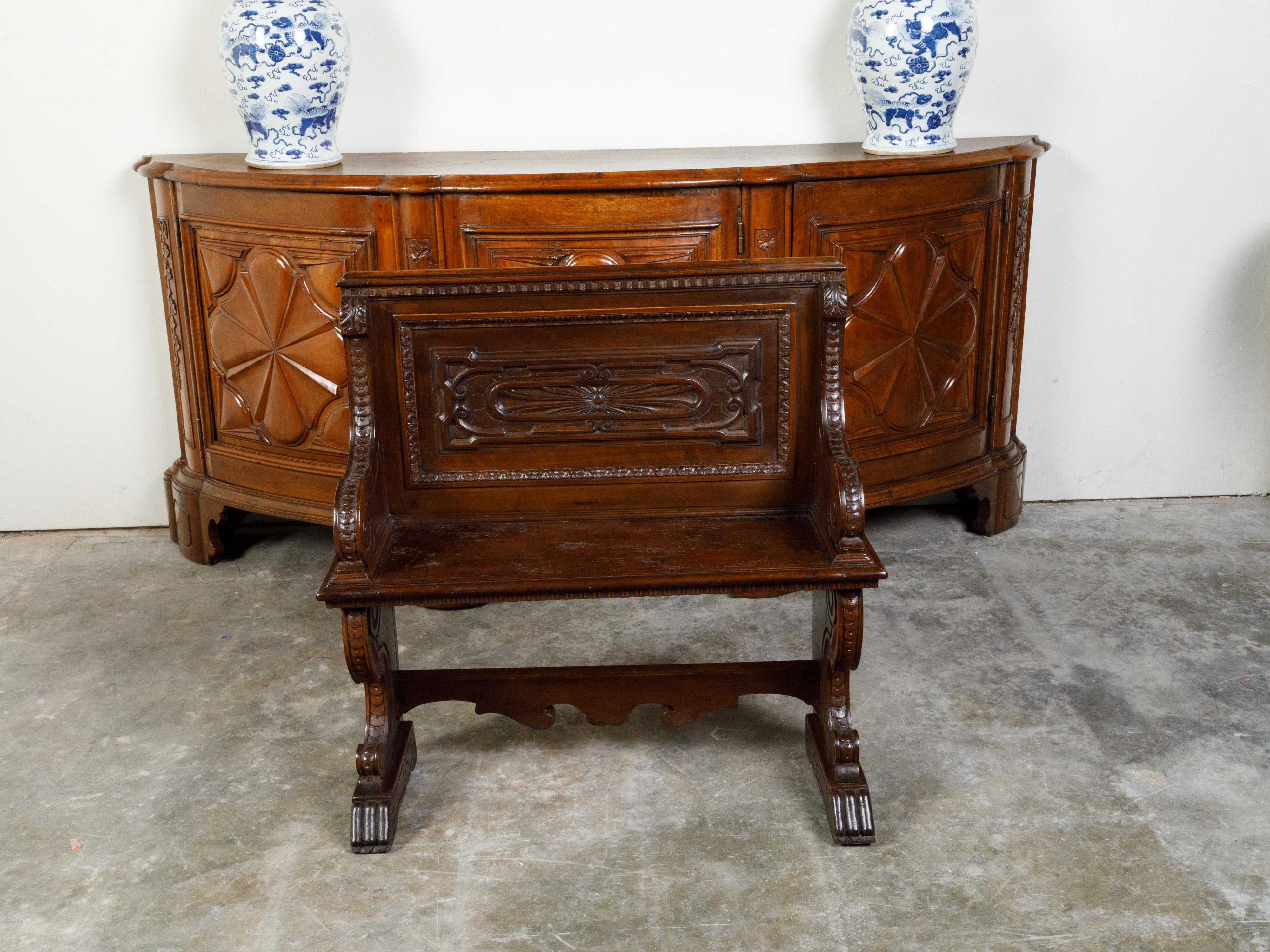 An Italian walnut hall bench from the 19th century, with carved back, voluted arms and stylized paw feet. Created in Italy during the 19th century, this walnut hall bench features a straight back with carved panel, connected to two large voluted