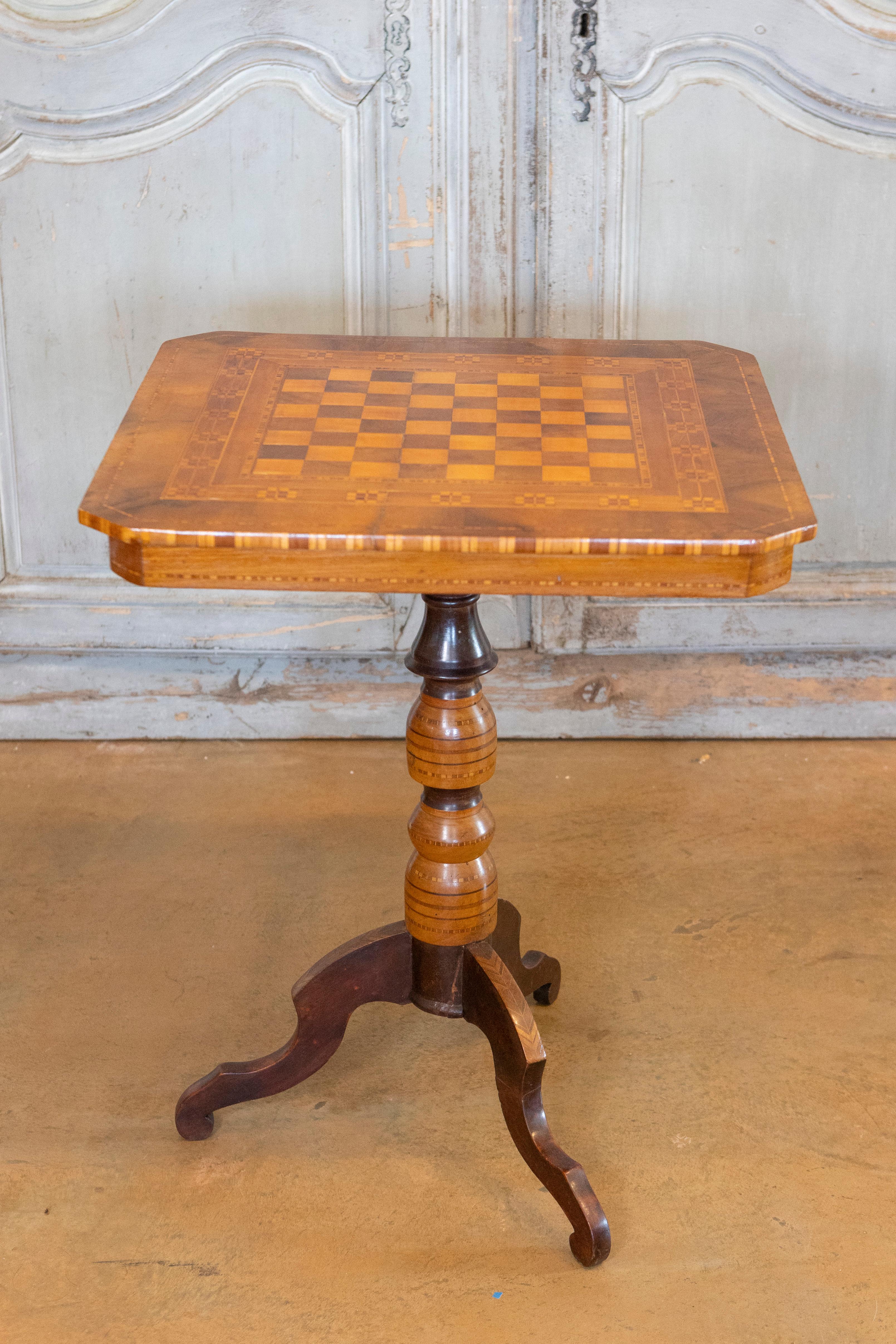 An Italian walnut, mahogany and ash game side table from the 19th century with marquetry top, turned pedestal and carved tripod base. This exquisite Italian game side table from the 19th century captures the eye with its masterful combination of