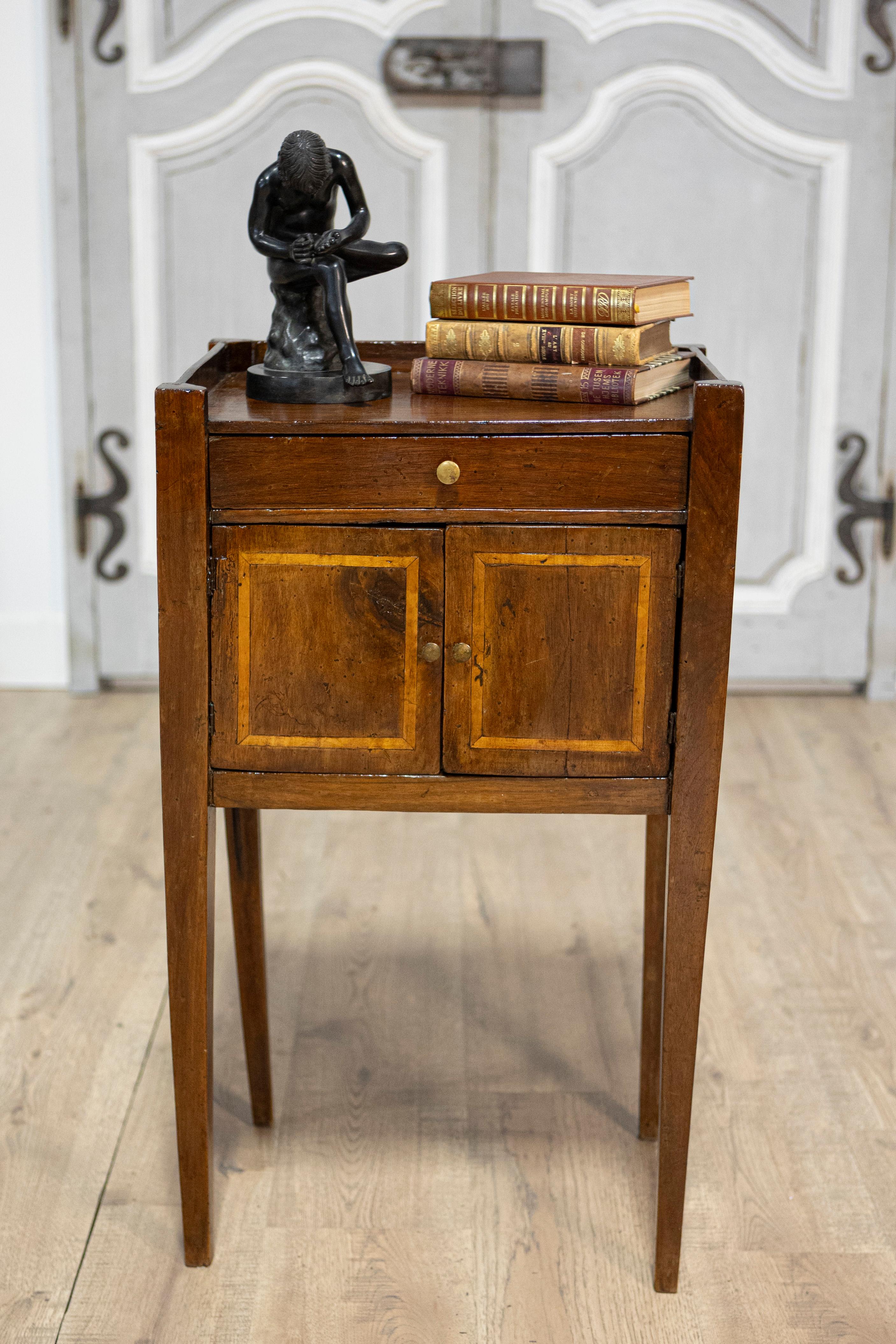An Italian walnut bedside table from the 19th century with ash banding, three-quarter wooden raised gallery, single drawer, double doors and tapered legs. Born in Italy during the 19th century, this charming walnut bedside table exudes a rustic