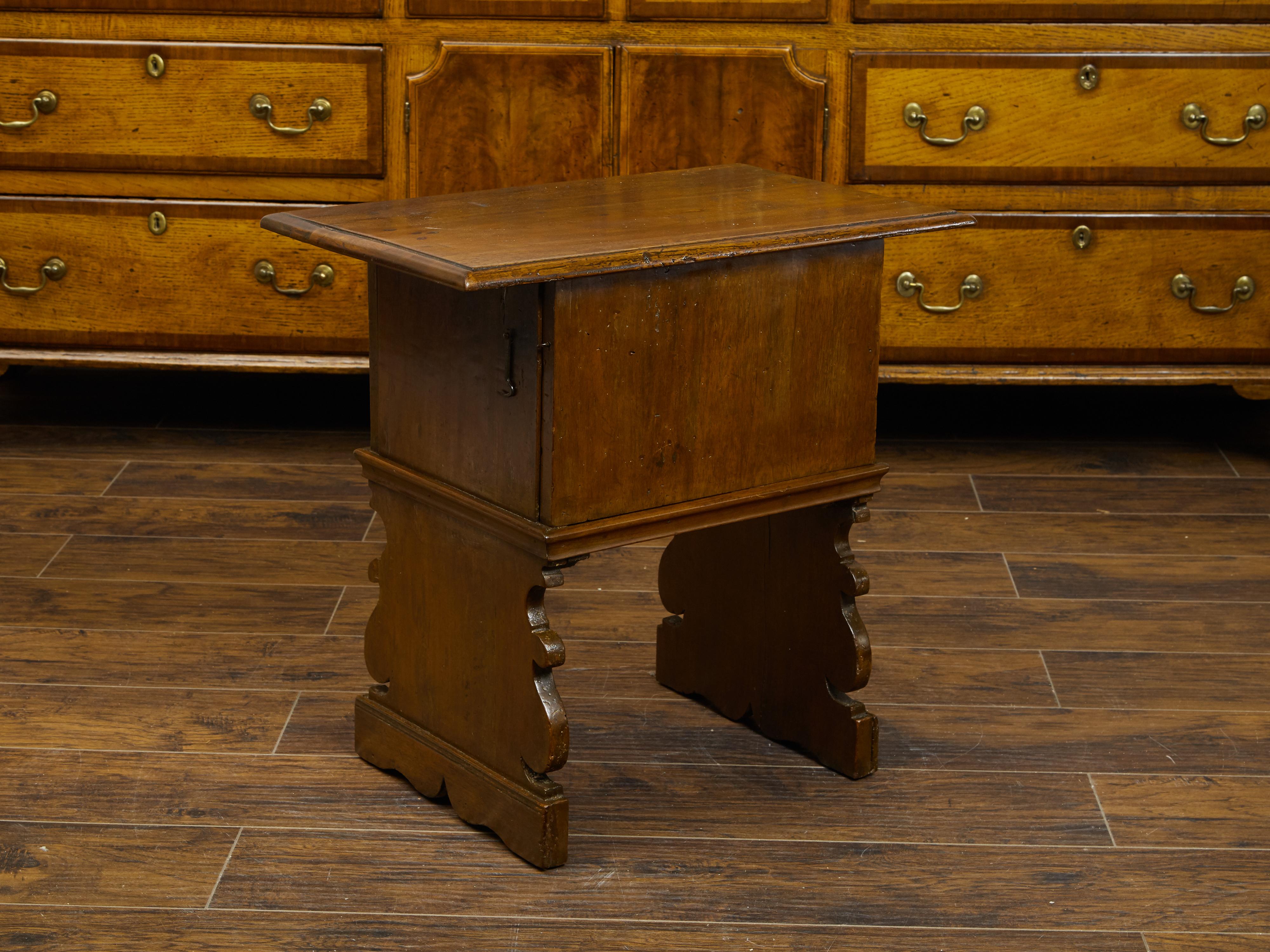 An Italian walnut side table from the 19th century, with single door and carved base. Created in Italy during the 19th century, this walnut side table features a rectangular top with beveled edges, overhanging a single door opening thanks to a