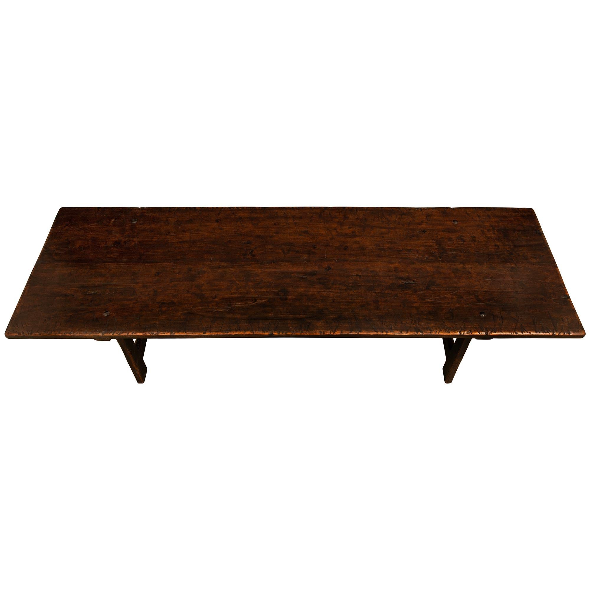 A handsome and large scale Italian 19th century Walnut trestle/dining table. The table is raised on four slanted tapered rectangular legs with straight and triangular shaped stretchers connecting the legs. Above is the solid Walnut rectangular top