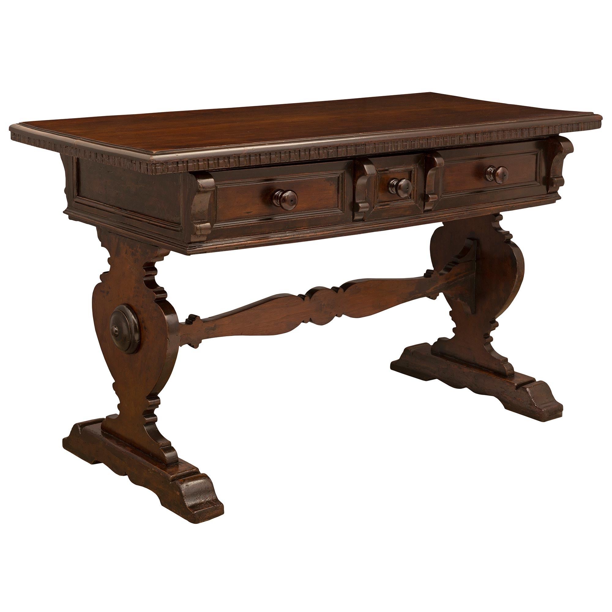 A very handsome Italian 19th century walnut trestle table. The table is raised on two carved supports joined by a carved stretcher. At the paneled frieze are three drawers with walnut pulls. All below the solid walnut top with dentil-style carved