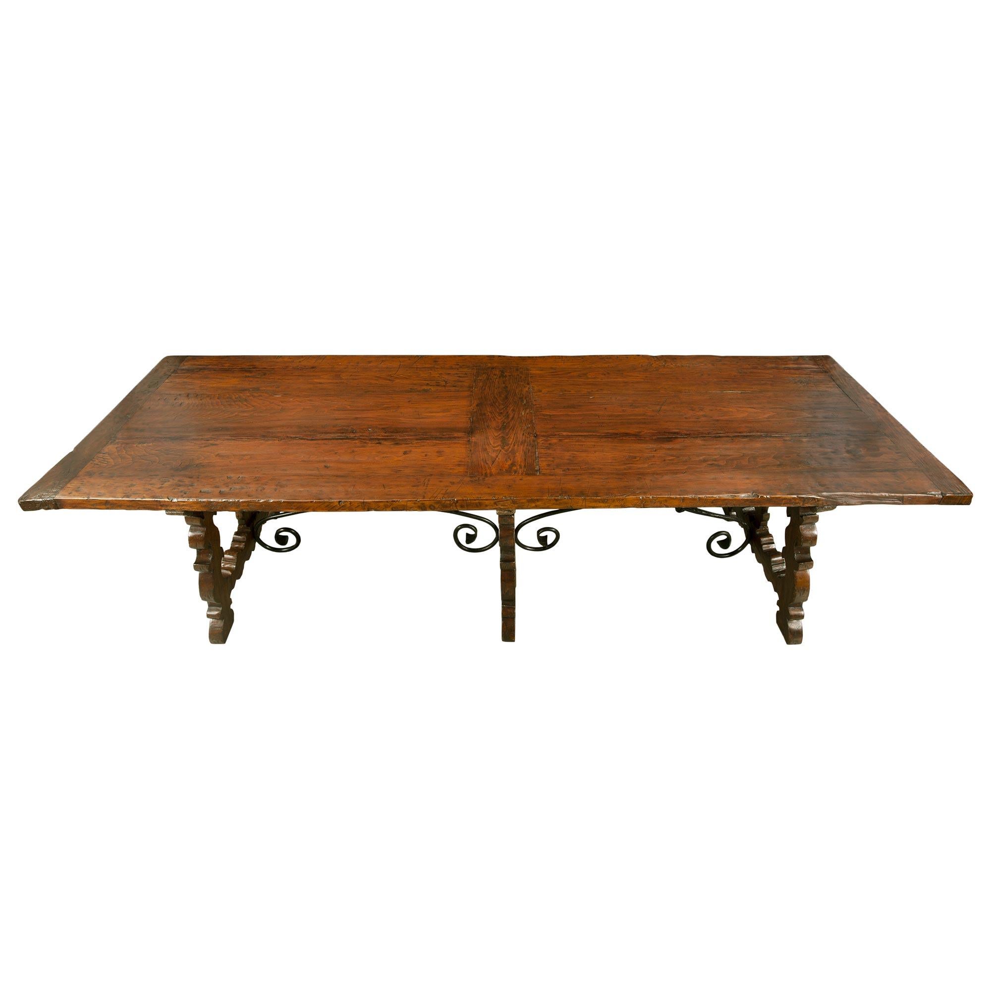 A unique and most decorative Italian 19th century walnut trestle table from Tuscany. The table is raised by three beautiful supports with fine carved scrolled foliate designs, X shaped iron mounts at each side and pegs. Each support is attached by