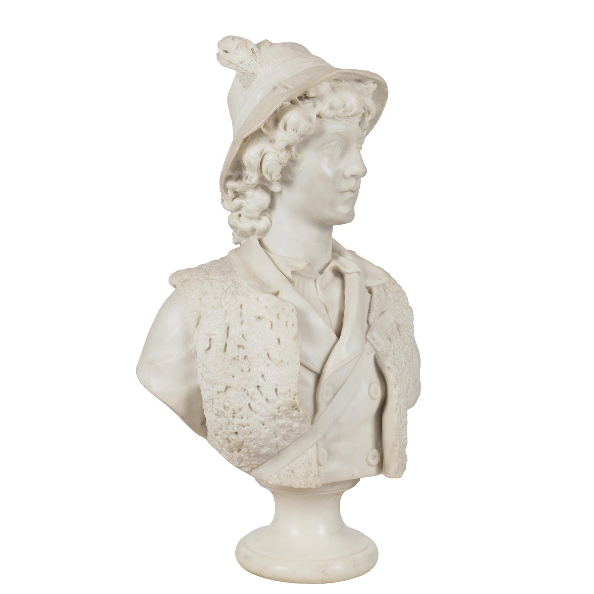 An impressive and wonderfully executed Italian 19th century white Carrara marble bust of a young hunter. The bust is raised by a circular mottled socle pedestal. The charming young man is wearing a shirt with a jacket and sheepskin gilet. He has a