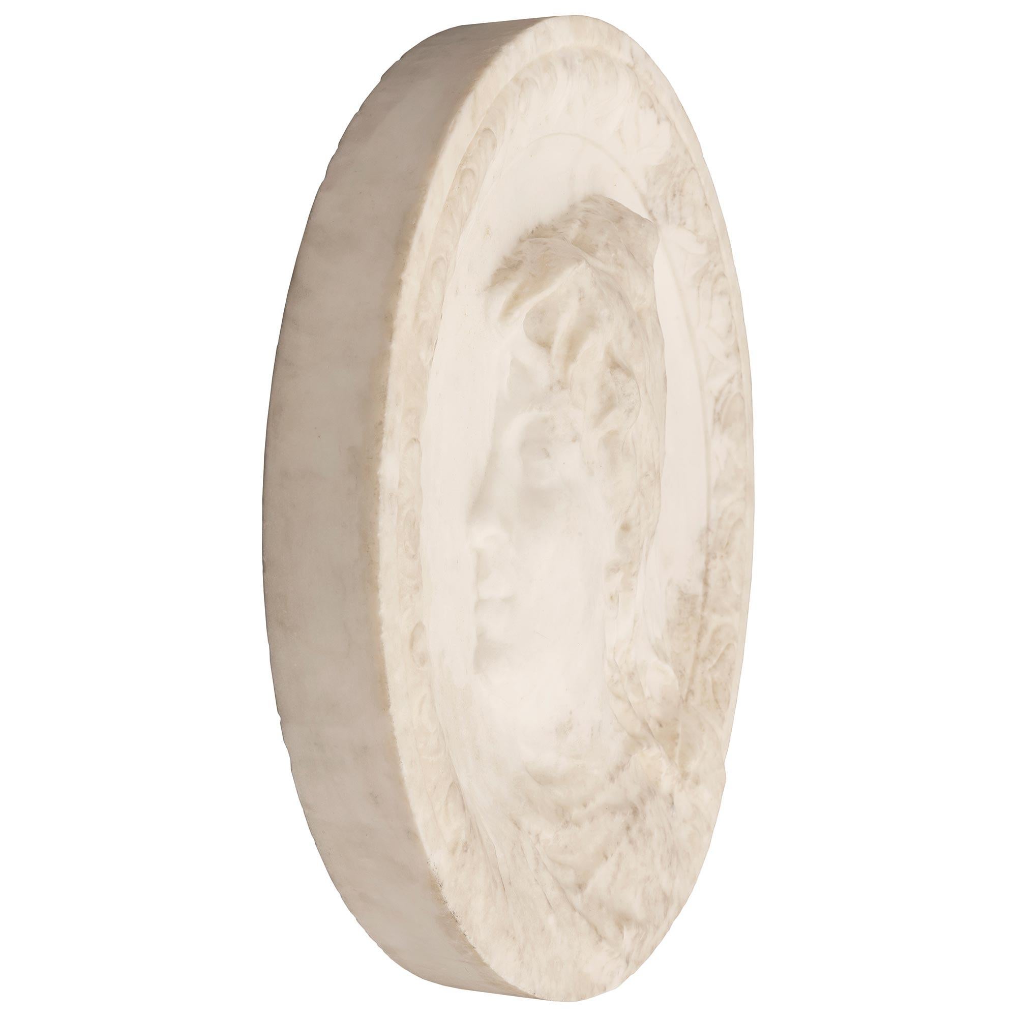 Remarquable plaque italienne en marbre blanc de Carrare du XIXe siècle. La plaque circulaire en marbre blanc massif de Carrare représente le profil d'un bel homme au chapeau, merveilleusement exécuté, encadré dans une charmante bordure feuillagée en