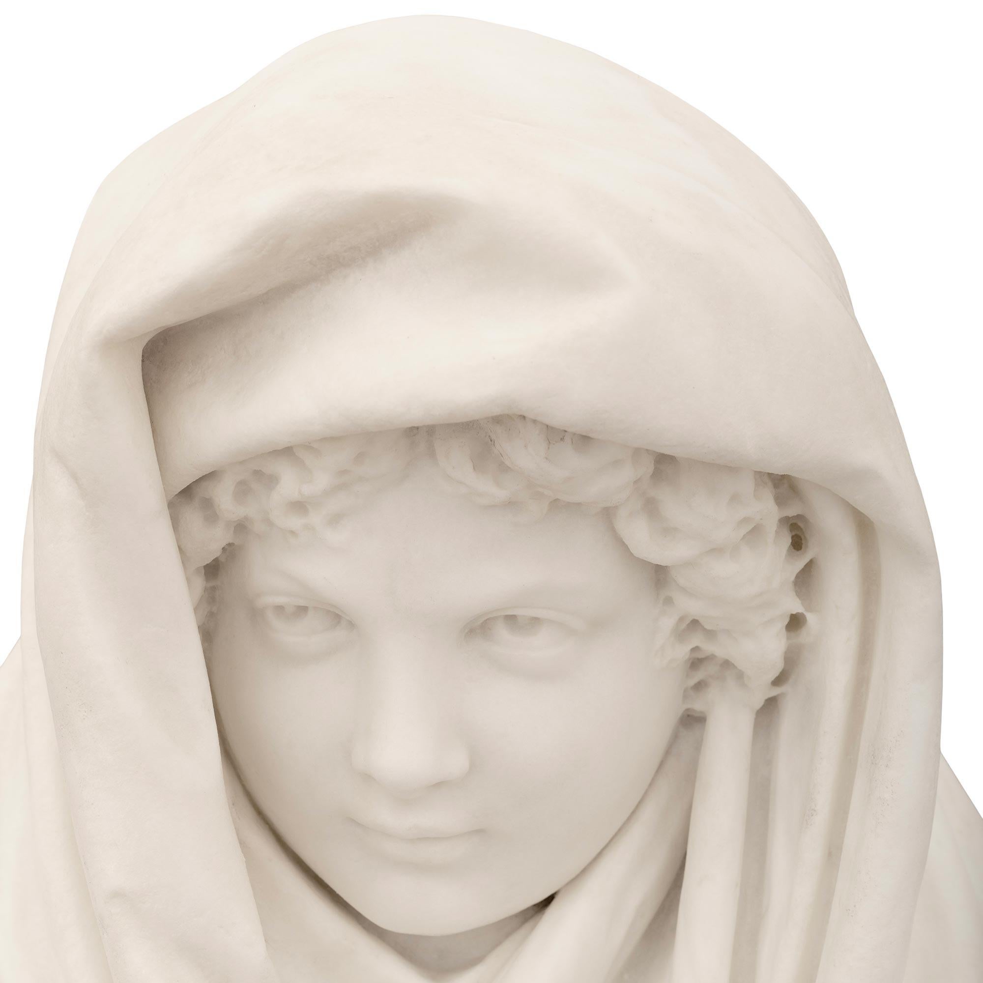 A finely executed and large scaled Italian 19th century white Carrara Marble sculpture of a young boy in a shawl. The boy is draped in a flowing oversized shawl which wraps around his shoulders and over his head. His exquisite facial expression and