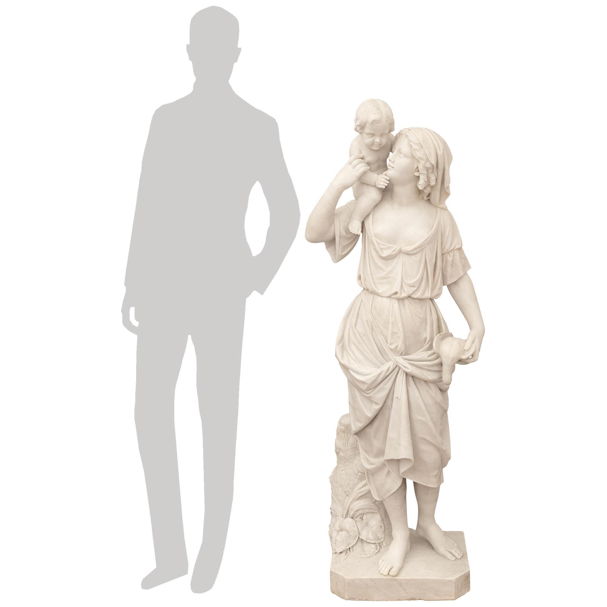 Una bella e imponente statua italiana in marmo bianco di Carrara del XIX secolo. Questa affascinante statua finemente scolpita poggia su una base quadrata in marmo con angoli tagliati e mostra una madre che porta il suo bambino sulla spalla mentre