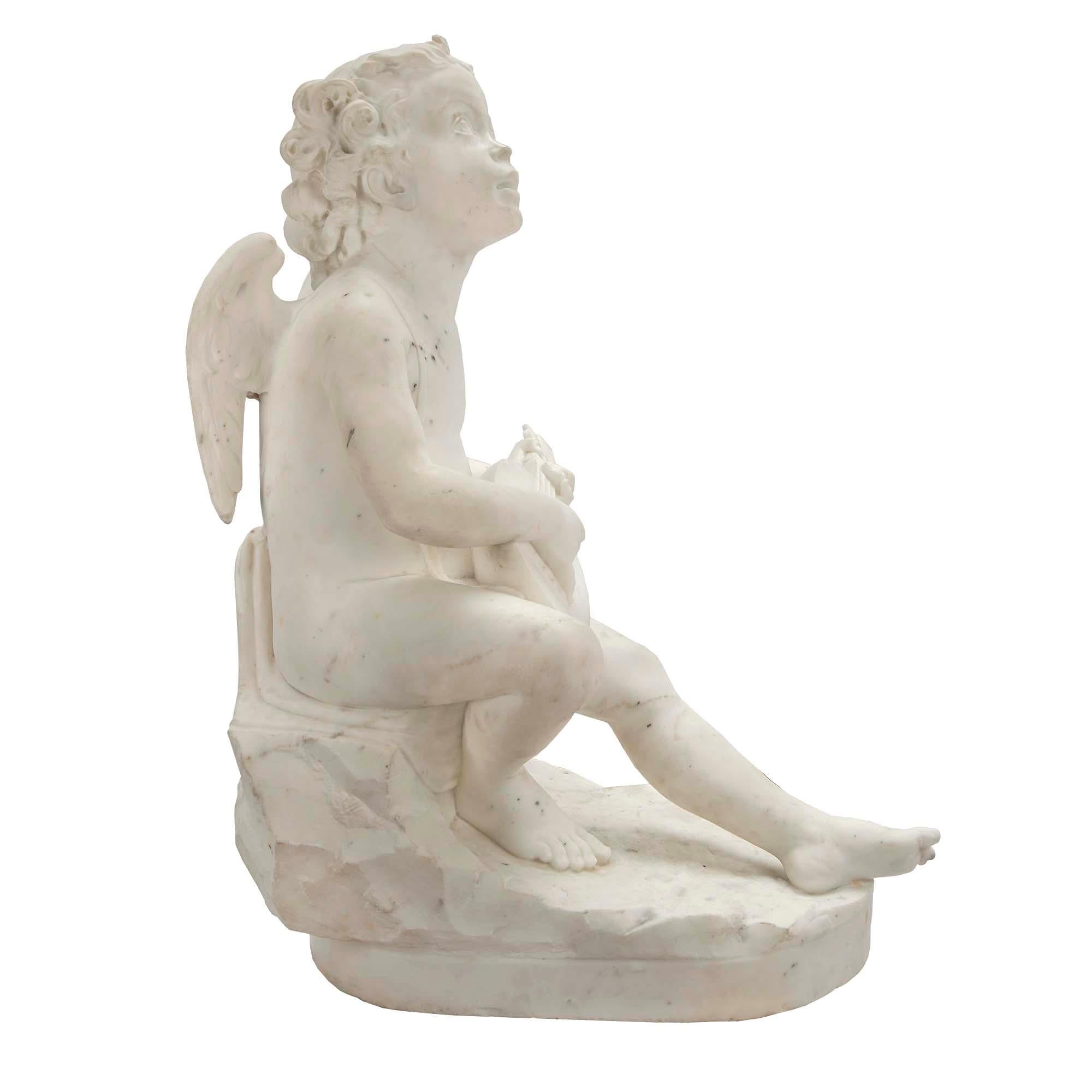 A charming and high-quality Italian 19th century white Carrara marble statue of a little winged cherub with his guitar. The statue is raised by an oval base with a rocky ground design, where the cherub is seated on a rock. He joyously looks up at