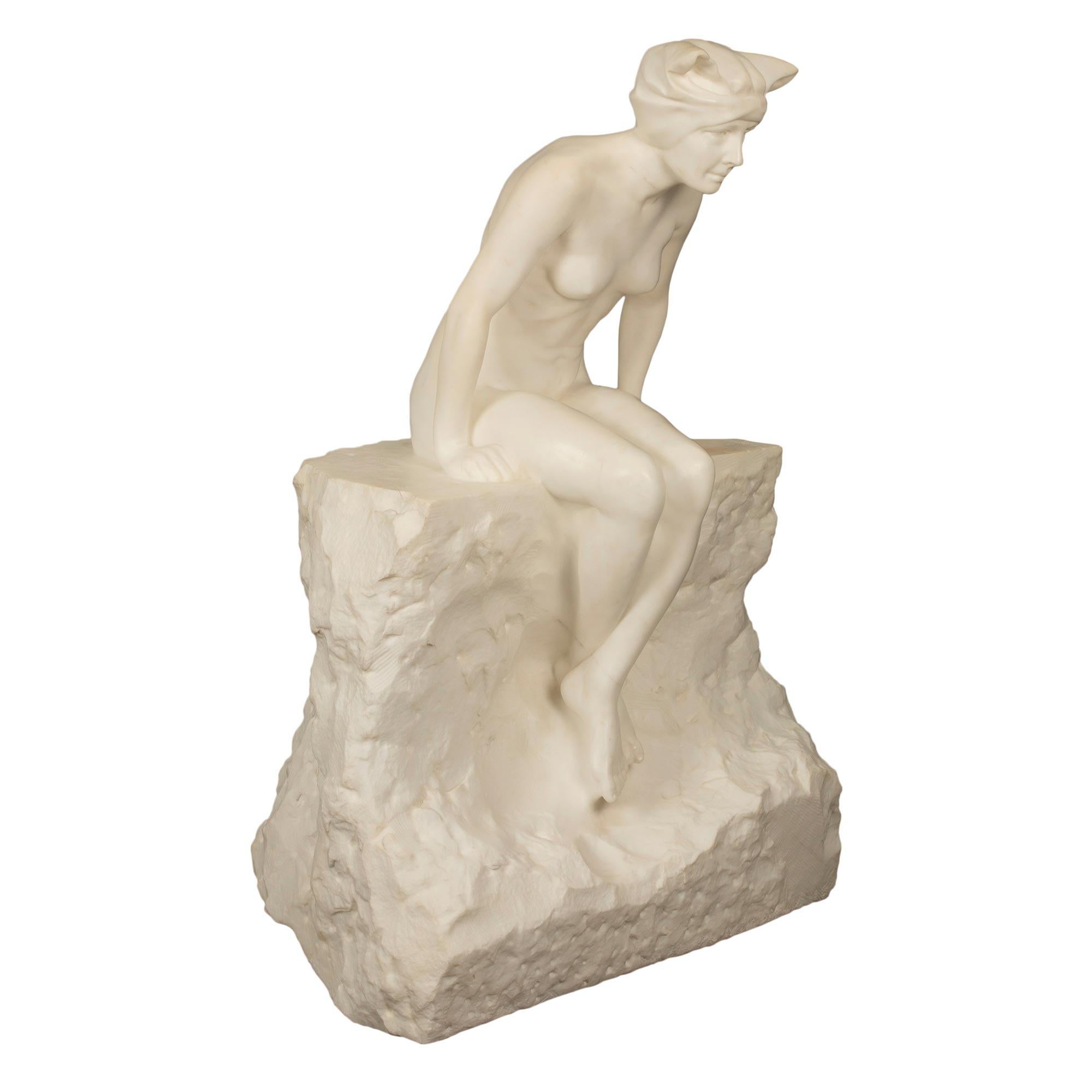 A striking Italian 19th century white Carrara marble statue of a maiden sitting on a rock. The statue is raised by a most impressive and large scale square rock designed base. The beautiful nude maiden wears a bathing bonnet and is seated on a rock,
