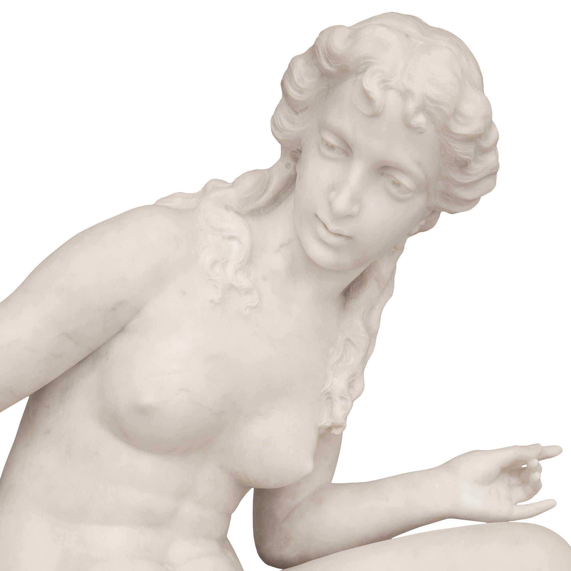 A charming and large scaled Italian 19th century white Carrara marble statue of a Venus and Cupid. The young Venus is seated on a rock with a flowing garment draped over her leg while gazing lovingly at the winged Cupid. She has one hand on her knee