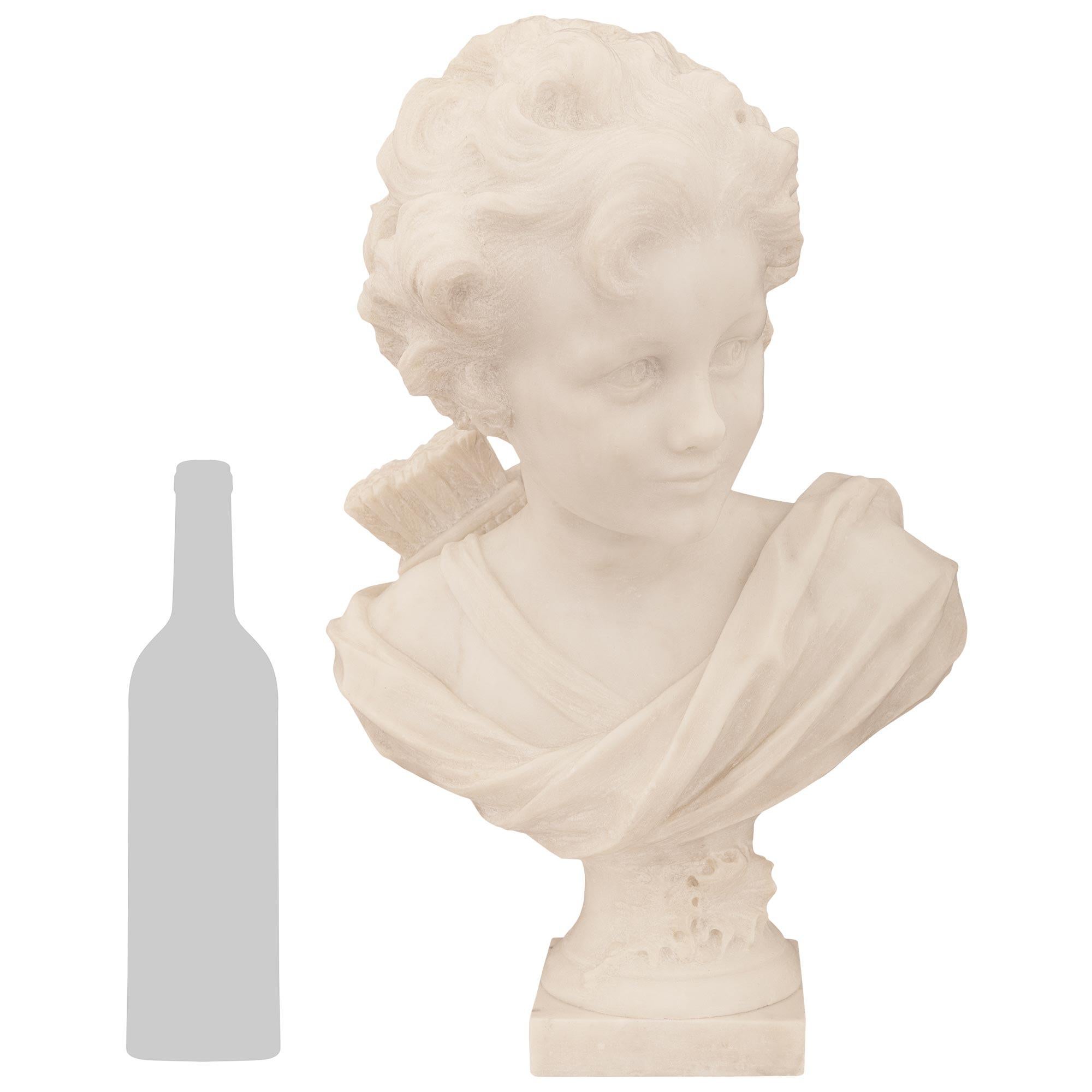 Un'affascinante statua di Cupido in marmo bianco di Carrara del XIX secolo, firmata A. Leonard. Questo bel busto è sollevato su un piedistallo a socle circolare decorato da intagli foliati e sostenuto da una base quadrata in marmo. Cupido è vestito