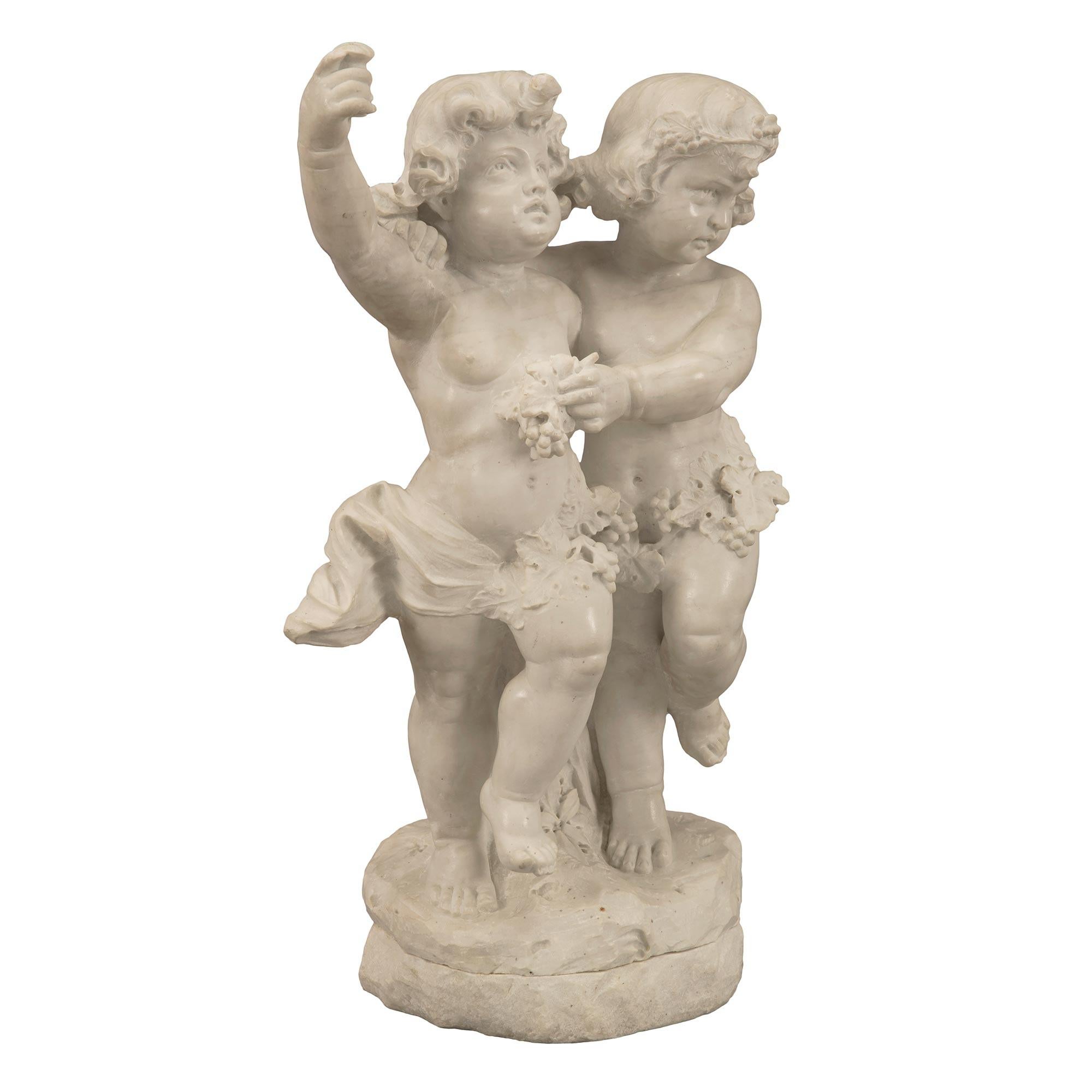 A charming and high quality Italian 19th century white Carrara marble statue of two children playing. The statue is raised by a circular base with a ground like design. Above are Bacchus and possibly Ariadne playfully dancing. Behind them is a