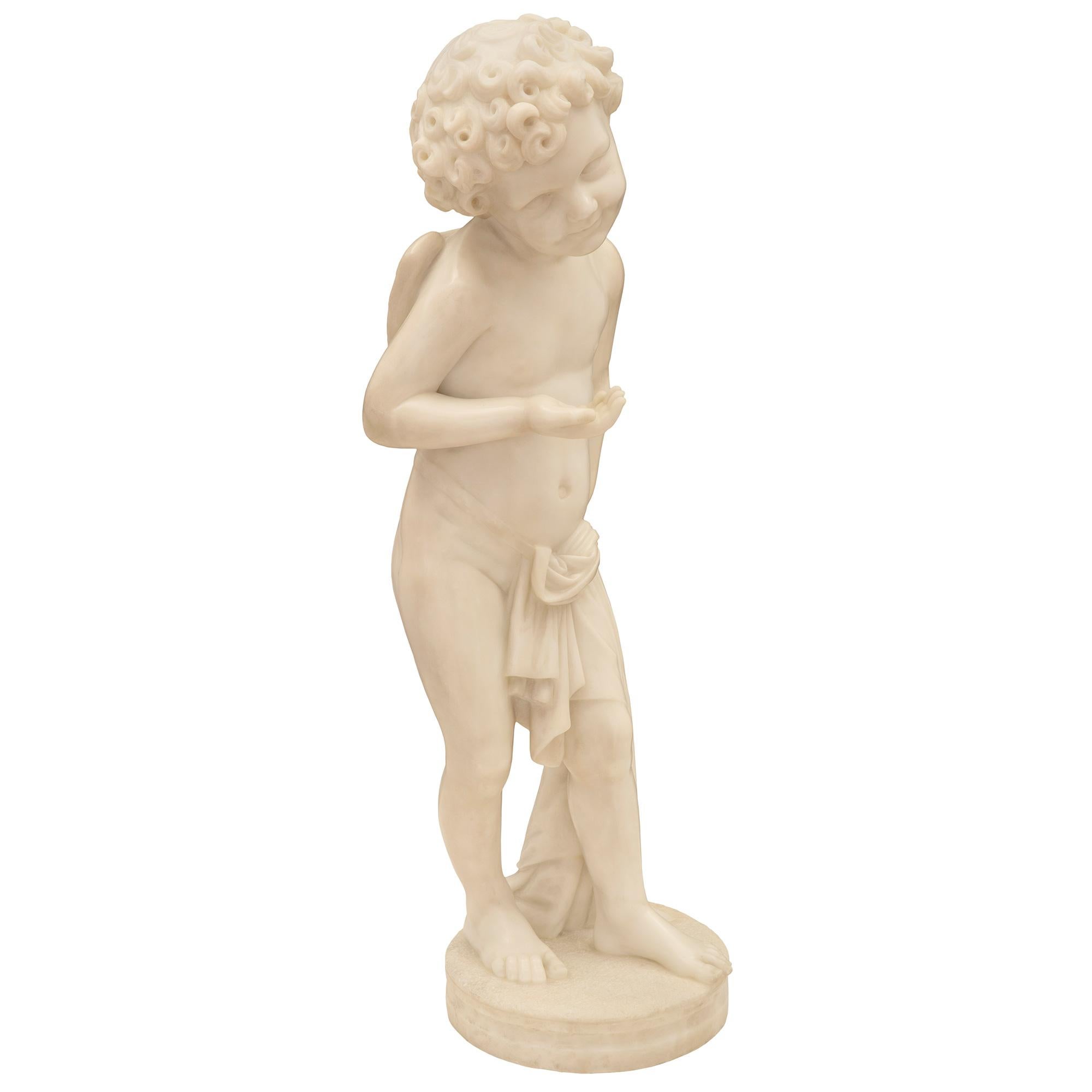 A most charming and finely detailed Italian 19th century white Carrara marble statue of young cupid. The statue is raised by a circular base with a fine wrap around mottled design. The wonderfully executed cupid is draped in a beautiful flowing
