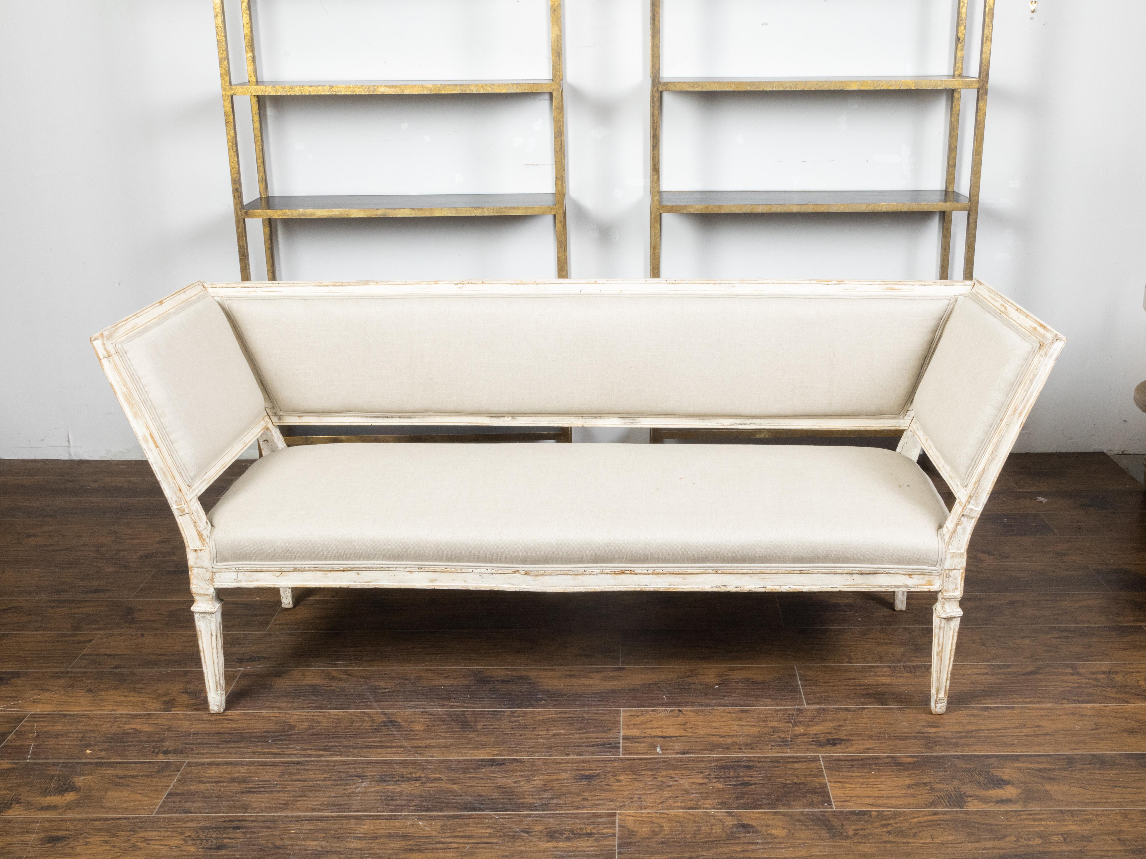 An Italian painted wood sofa from the 19th century, with two slanted sides, tapered carved legs and distressed patina. Created in Italy during the 19th century, this painted sofa features a straight back connected to two slanted sides, surrounding a