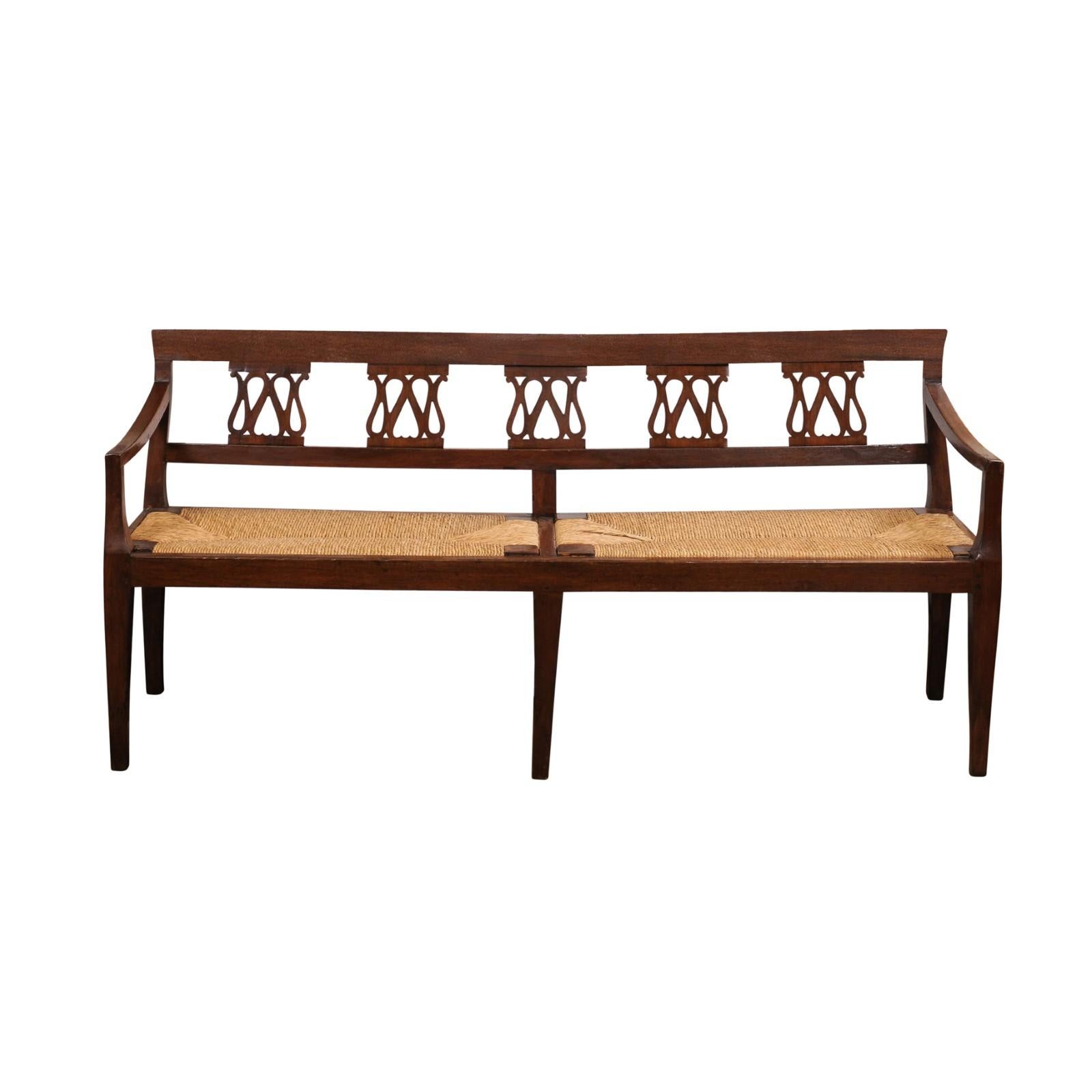 An Italian walnut bench from the 19th century with carved splats, rush seat and tapered legs. This 19th-century Italian walnut bench is a testament to classic craftsmanship and timeless style. The bench features beautifully carved splats, showcasing