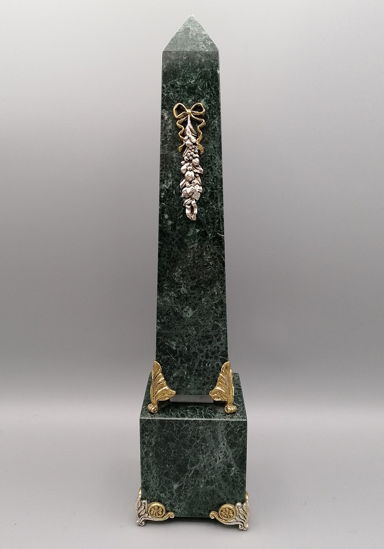 Green marble obelisk with sterling silver friezes.
The frieze on the obelisk depicts a composition of fruit with a love knot and is placed on a base, again in green marble, on 4 feet in two-tone, natural and gilded solid sterling silver.
The base