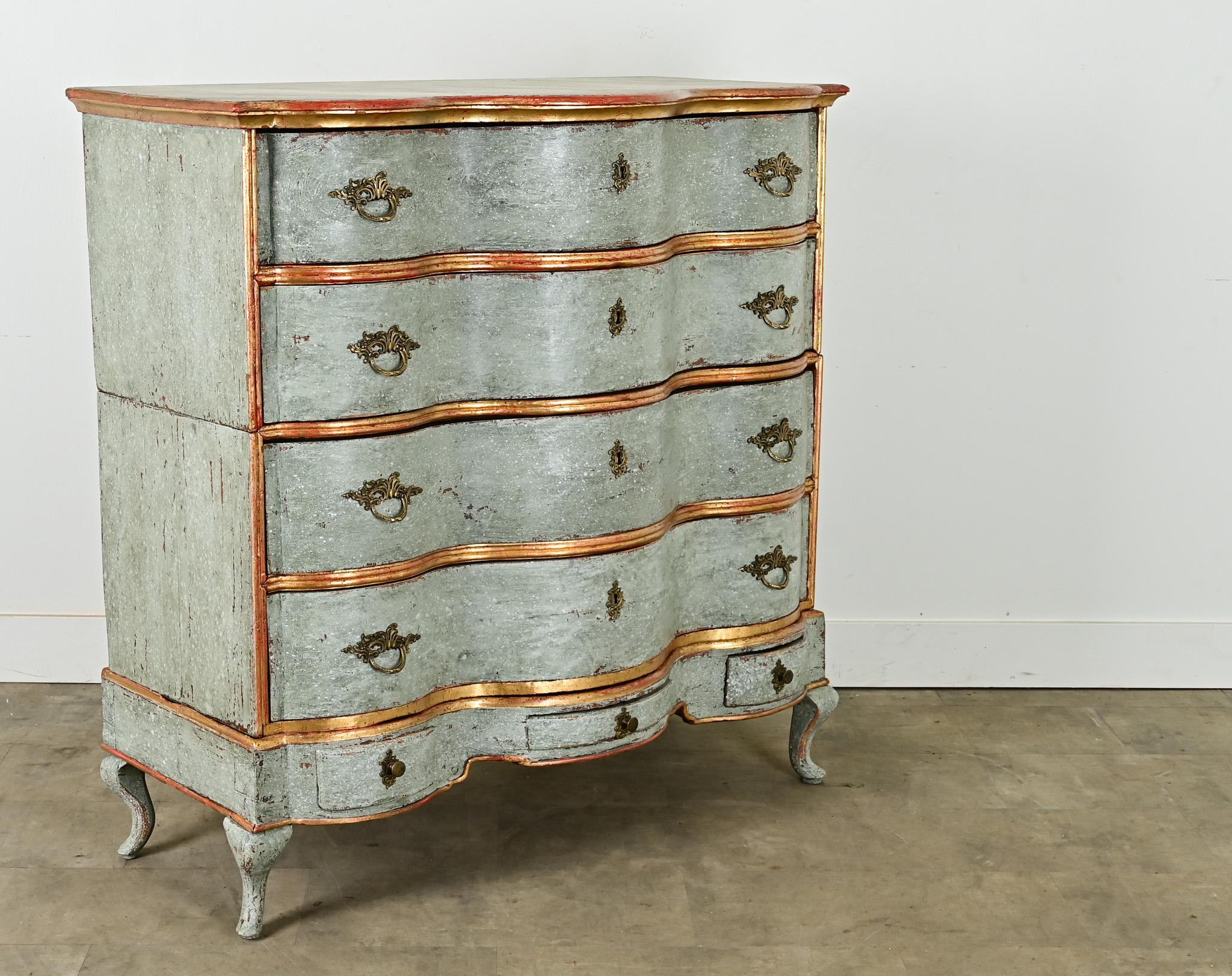 Una majestuosa cómoda italiana tiene una fachada flamígera y festoneada, con su acabado original de pintura azul en capas y adornos dorados. La encimera de mármol de imitación está encima de una cómoda con siete cajones de distintos tamaños, todos