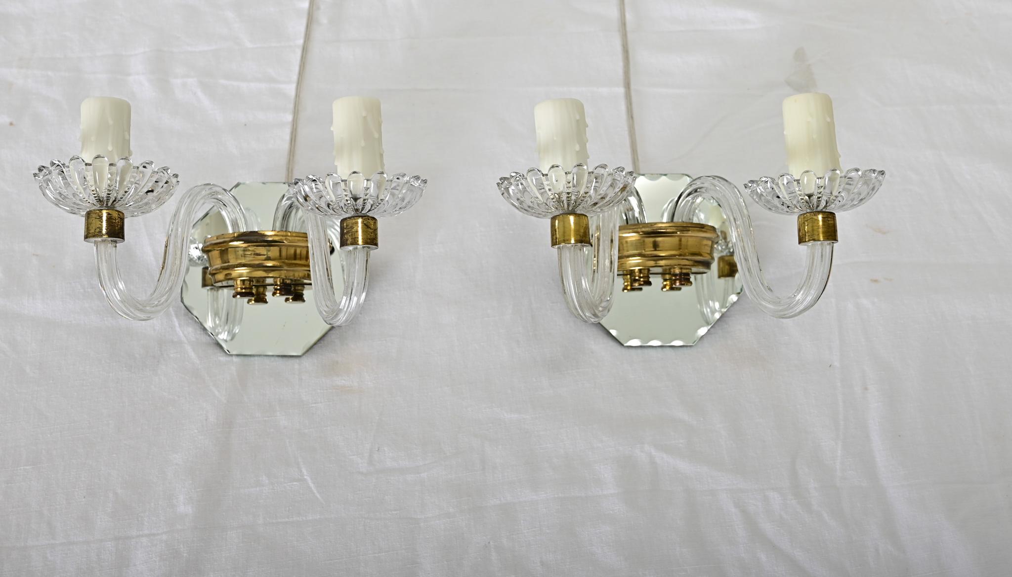 Una piccola coppia di applique italiane del 1930 circa in vetro trasparente, vetro a specchio e ottone. Ogni applique presenta una coppia di bracci con finte coperture di candele per lampadine a candelabro, che si ergono da bobeche in vetro pressato