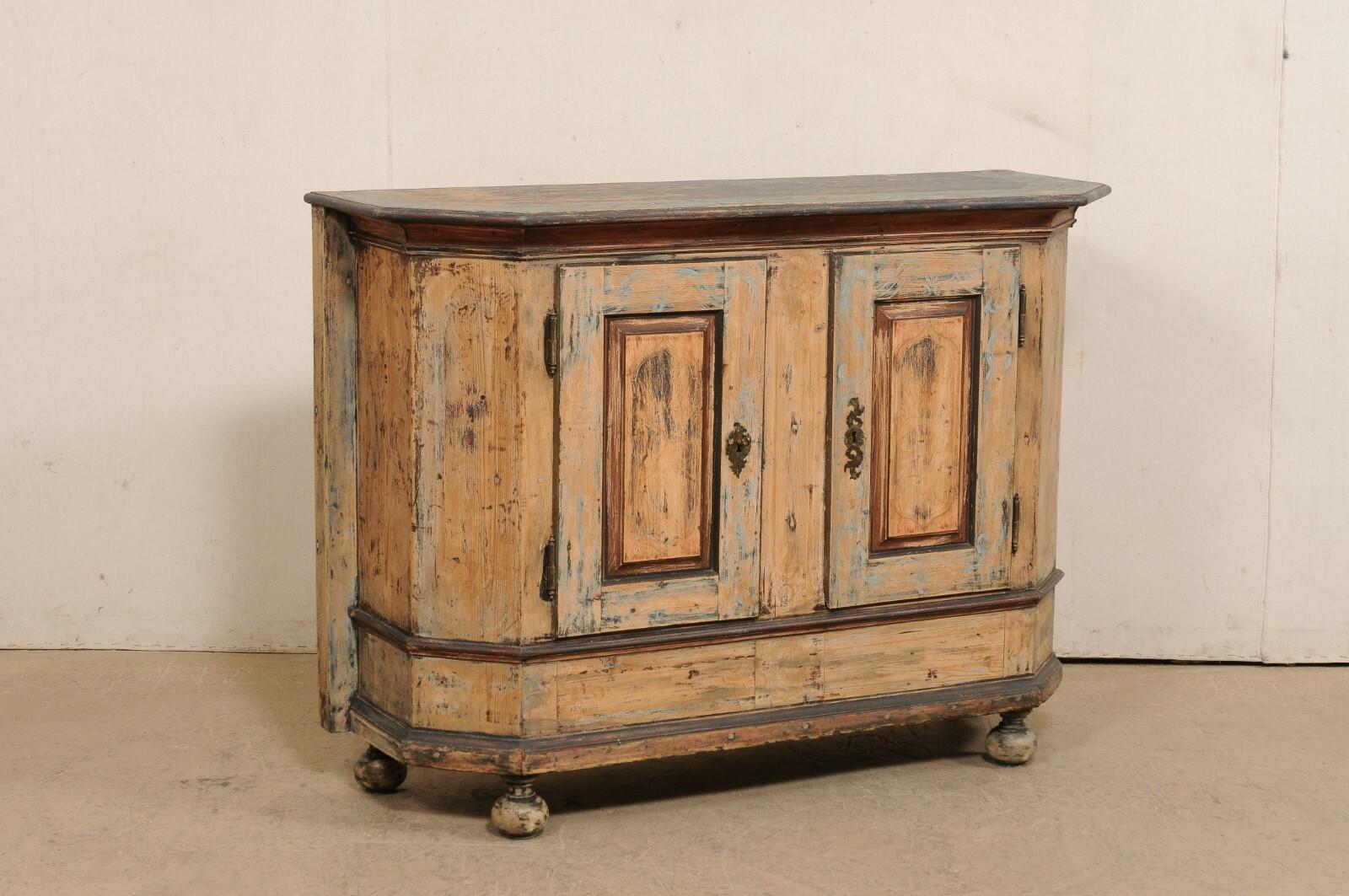 An Italian console cabinet from the early 19th century (possibly older). This antique chest from Italy from features a shorter front side which gives way to two chamfered sides, and an elongated backside (meant to be placed against the wall). The