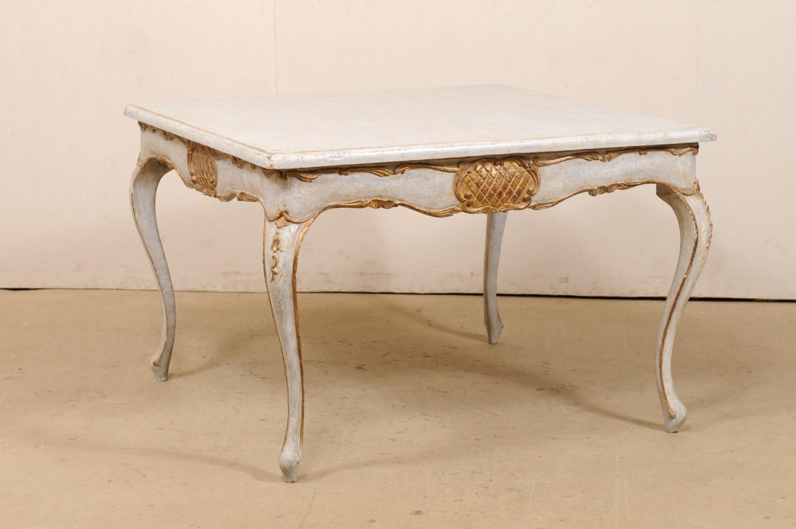 A vintage Italian square-shaped carved-wood table with gilt accents. This painted wood table from Italy features a square-shaped top with softly, rounded corners, a scalloped skirt which is adorn with carvings highlighted in a gilt finish, and is