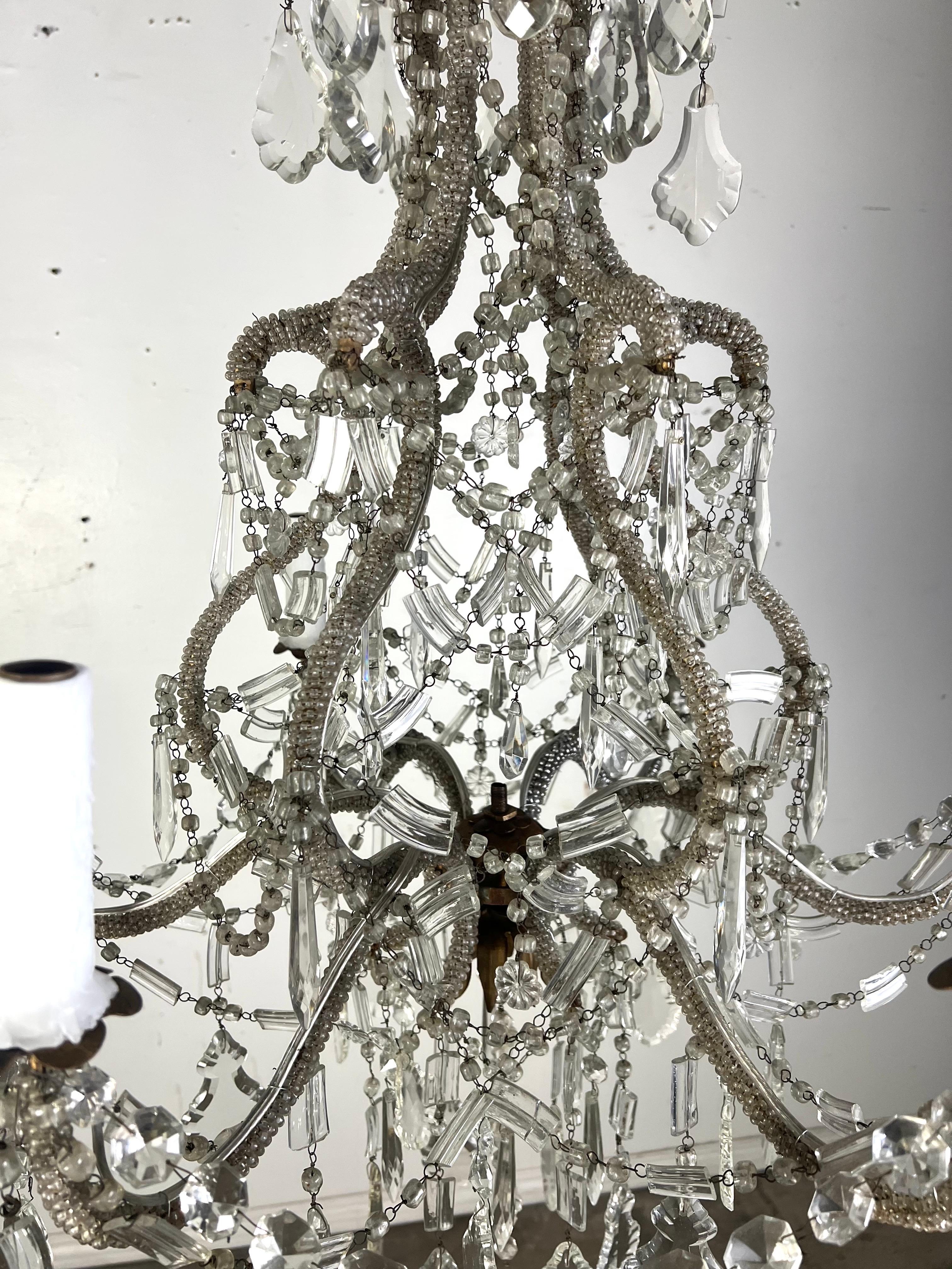 Lampadario italiano a sei luci in un elegante apparecchio decorato con cristalli dal design classico e ornato.  La sua struttura in metallo è intricatamente decorata con fili di piccole perline che ricoprono i bracci curvi e gli elementi