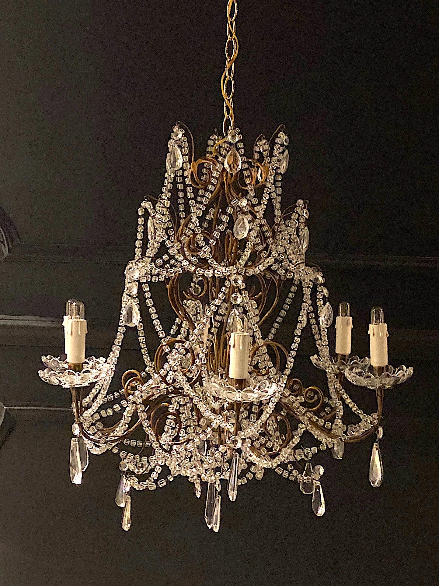 A charming Italian 1950s Hollywood Regency style gilt iron and glass bead and crystal chandelier. The body of the chandelier measures 24 inches in diameter and 24 inches high. There are six arms with candelabra sockets and scallop glass bobeches.
