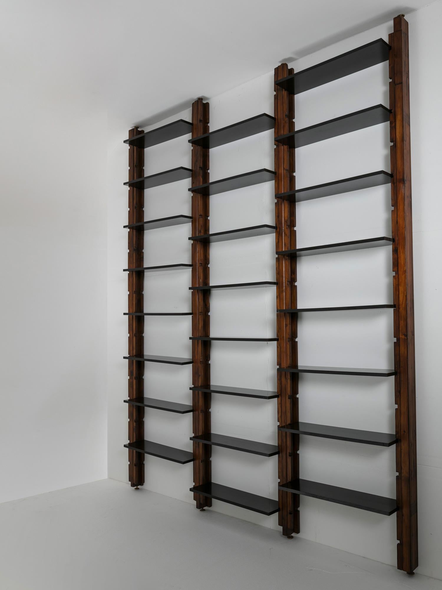 Large modular bookcase composed by movable black painted shelves and wood uprights with brass feet. More uprights and shelves available.