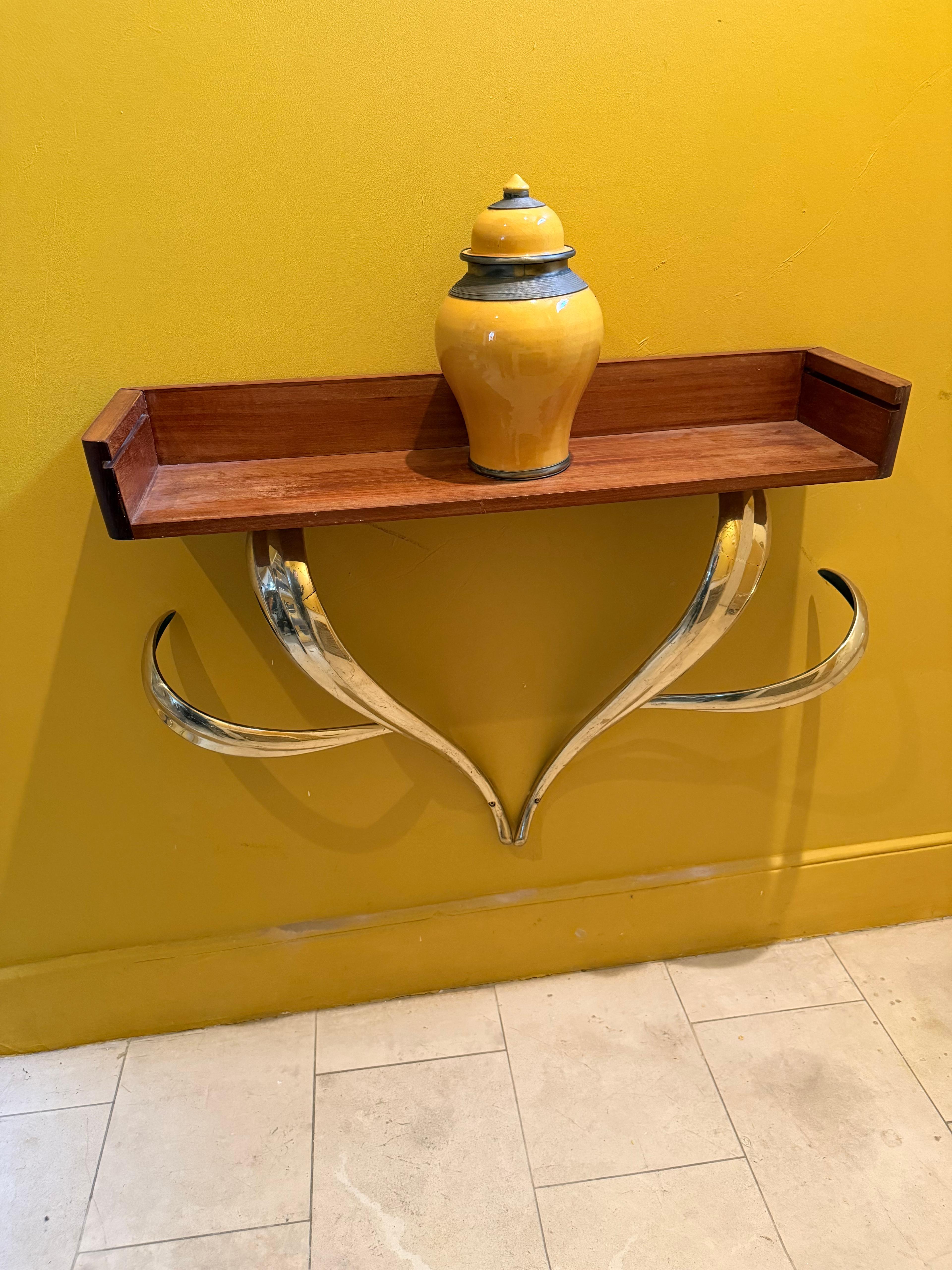 This item is a console table or wall mounted with a sliding glass shelf (Glass shelf is missing, but we can cut it if require) shelf with a distinct Art Deco or Mid-Century Modern style, featuring a wooden top and sculptural, curved brass plated