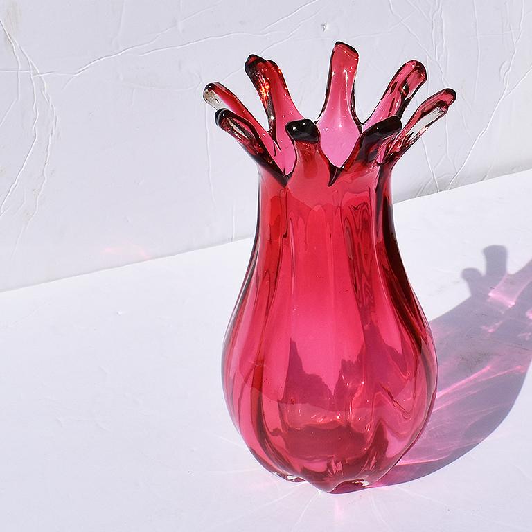 A bright berry red color curvy tall Murano glass vase. With a wide base, cinched top, and sprawling scalloped finger-like lip, this vessel is a true statement piece. The base is rounded, as is the entire vessel. Sculptural dips in the glass run