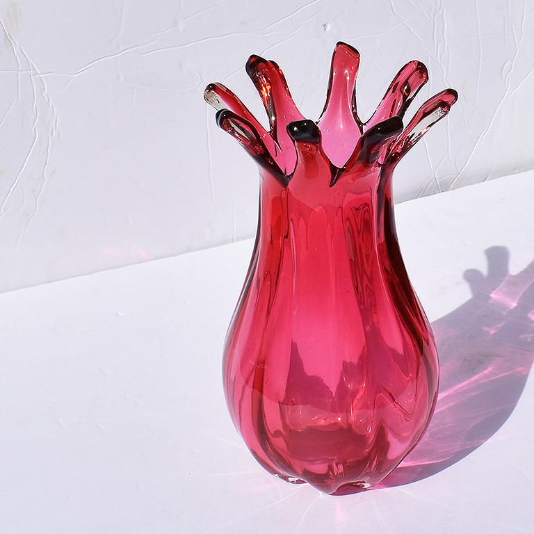 Eine leuchtend beerenrote Farbe geschwungene hohe Vase aus Muranoglas. Mit seinem breiten Sockel, dem geschwungenen Oberteil und der ausladenden, fingerartigen Lippe ist dieses Gefäß ein echtes Statement. Der Boden ist abgerundet, ebenso wie das