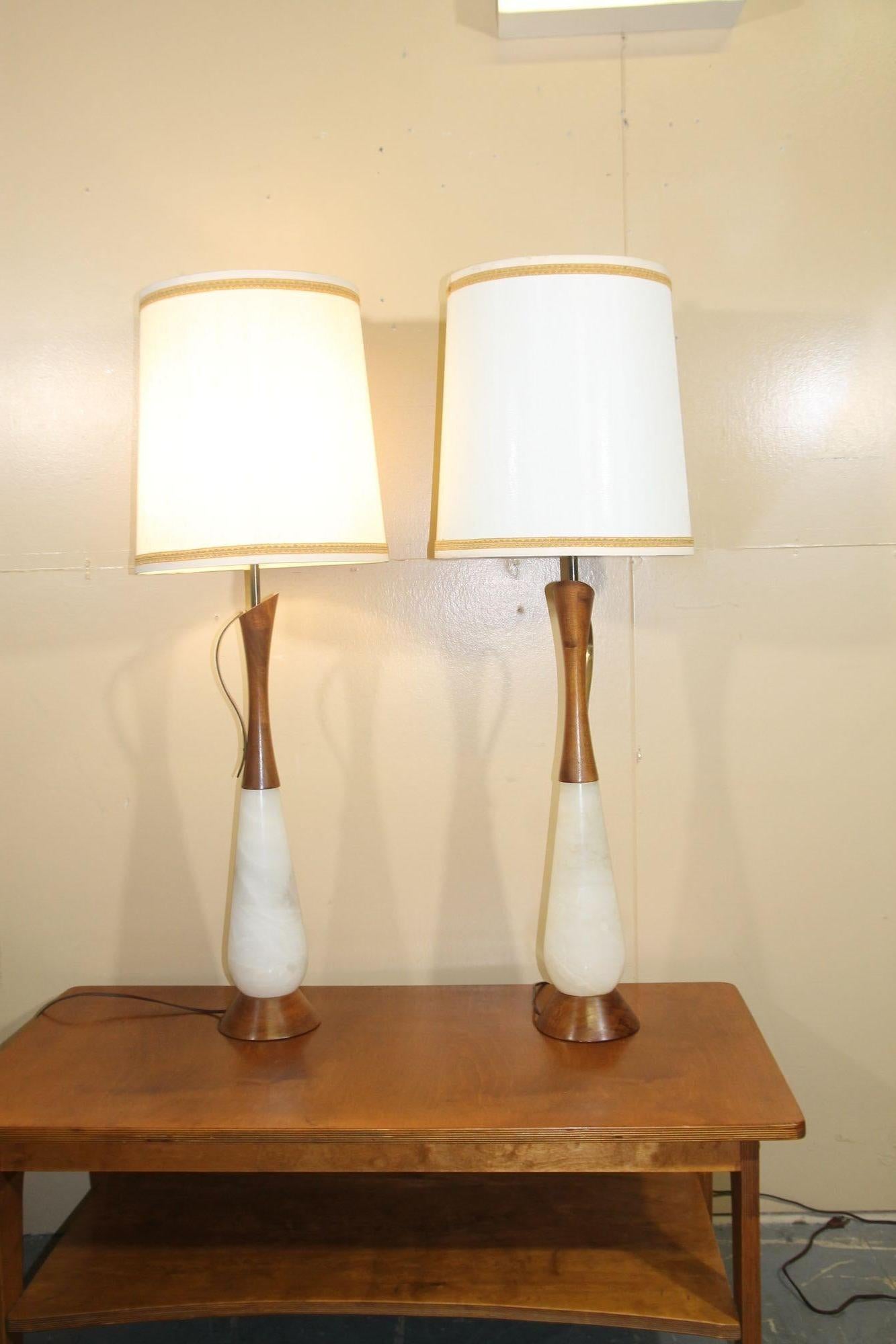 Pleased to offer this great pair of Italian table lamps. These alabaster lamps have walnut base and top as well as brass handle. These lamps retain their original shades and alasbaster finials. This pair of lights will look amazing in any decor.