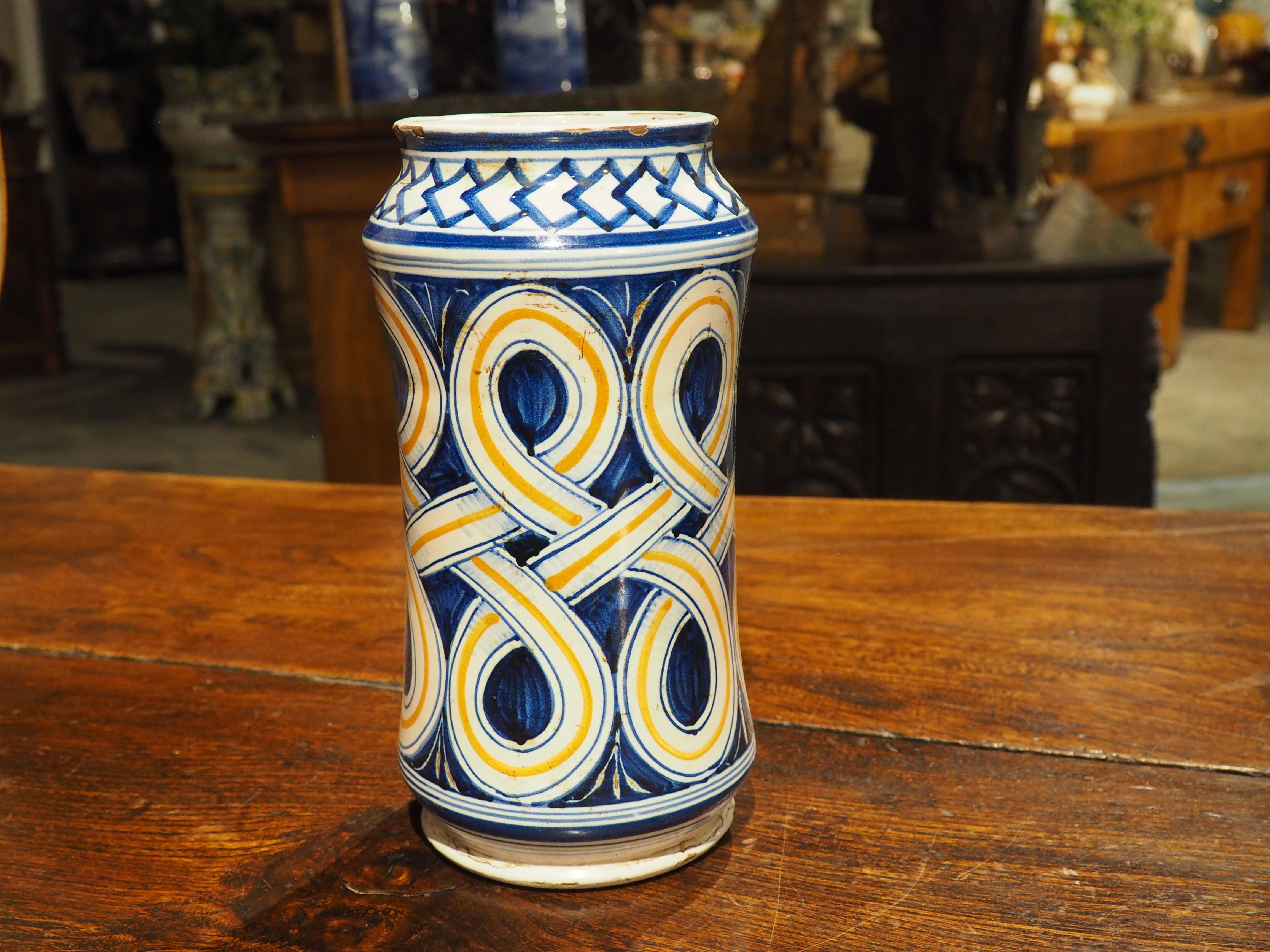 Los motivos de bandas entrelazadas de este tarro italiano de albarelo son bastante hipnóticos. Pintado a mano en el siglo XIX, este recipiente de mayólica para boticario tiene un arabesco de bandas blancas, parcialmente rellenas de líneas naranjas.