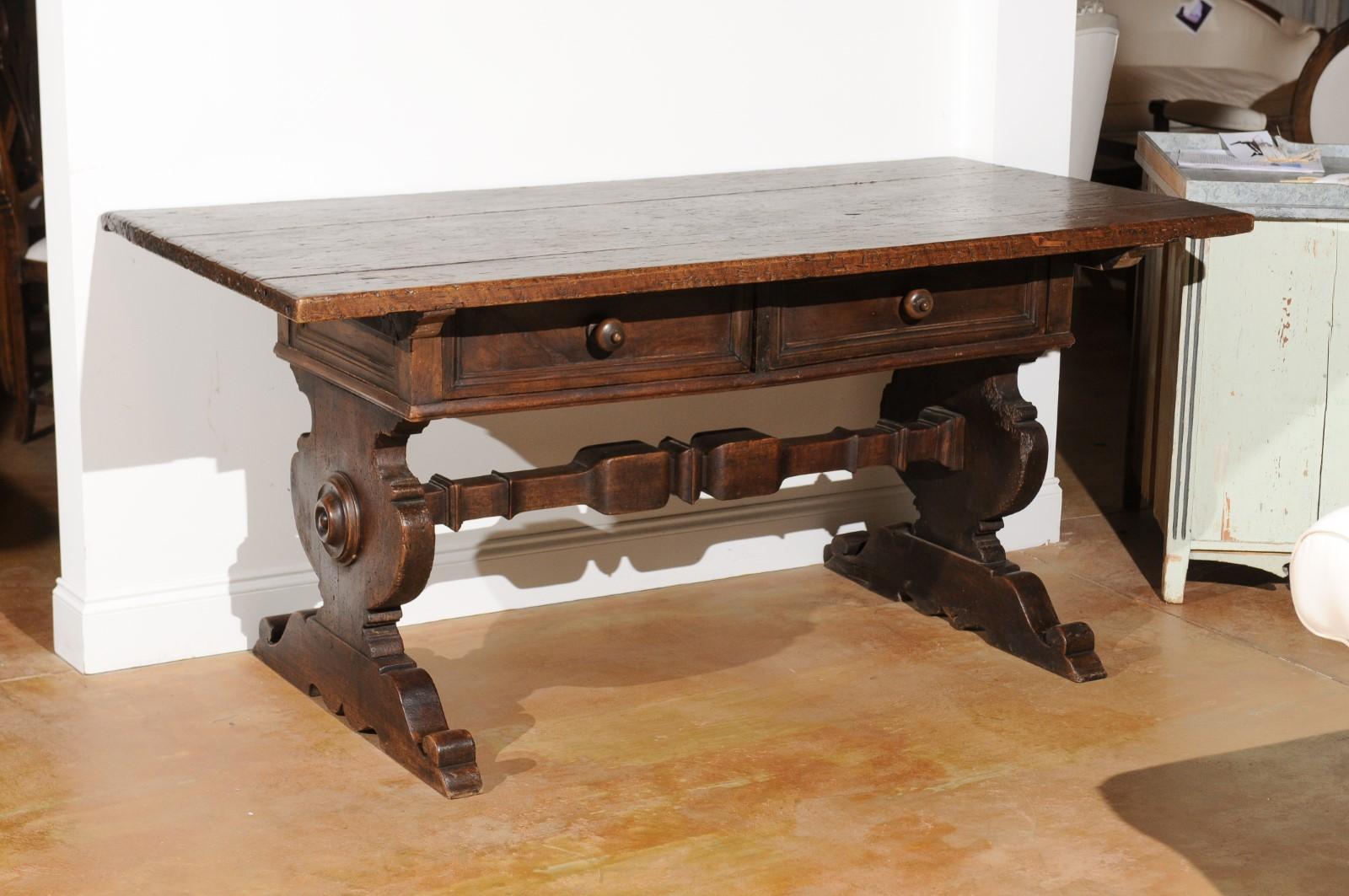 An Italian Baroque style 19th century walnut table from the Italian Alps with drawers and trestle base. Born in the Italian Alps during the 19th century, this exquisite table features a rectangular planked top sitting above two drawers fitted with