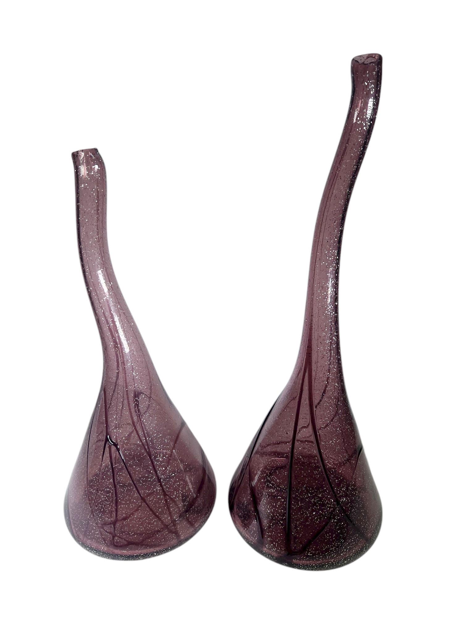 A striking pair of Italian glass vases in a rich amethyst hue, showcasing both elegance and versatility. The pair features varied heights, one standing at 21 inches, the other at 18 inches, creating a graceful, complementary display.

The deep
