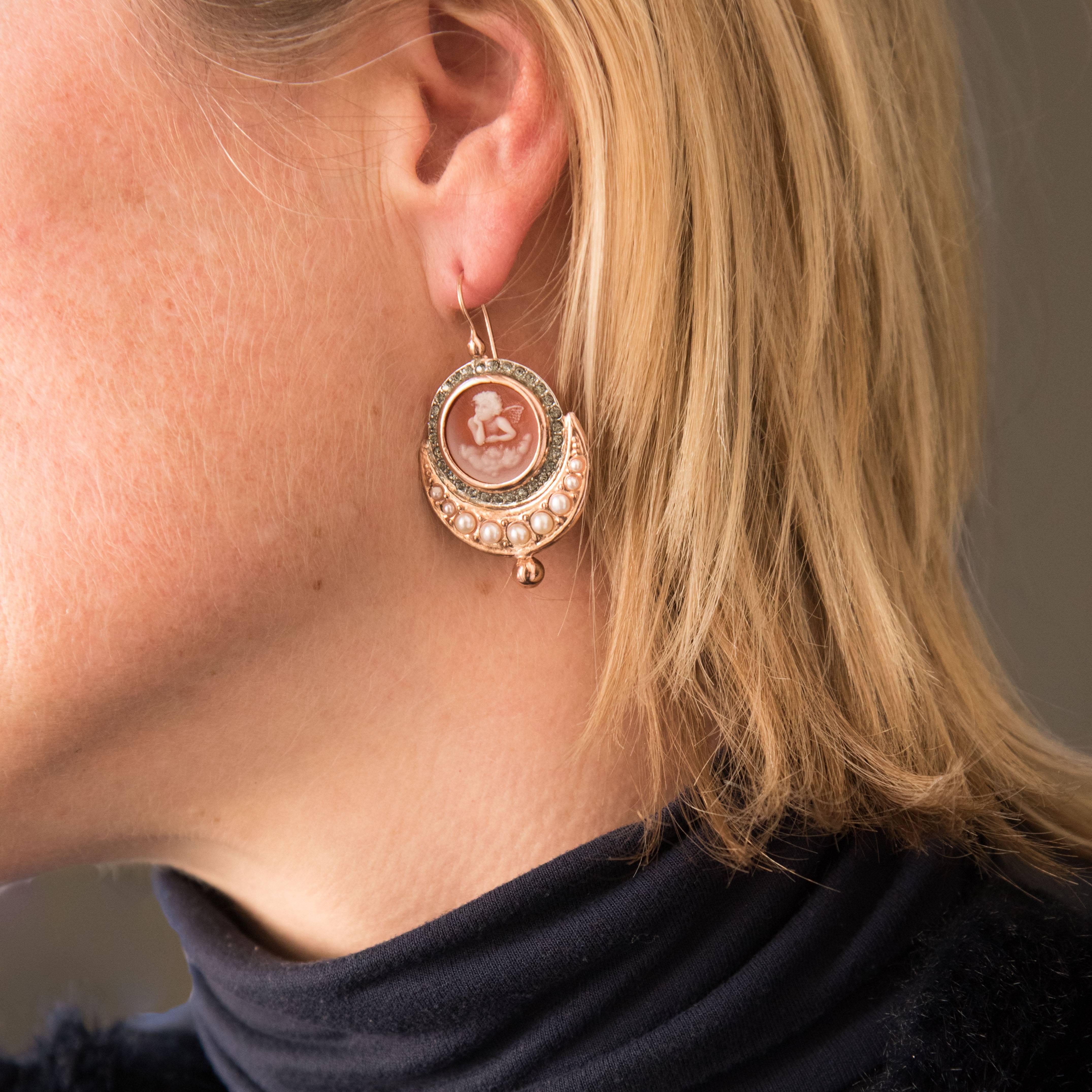 For pierced ears.
Pair of dangling earrings in silver and rose gold.
They are set with a cameo on glass paste surrounded by crystals. A line of falling glass pearls supports this decor and ends with a gold pearl. The fastener is a gooseneck with