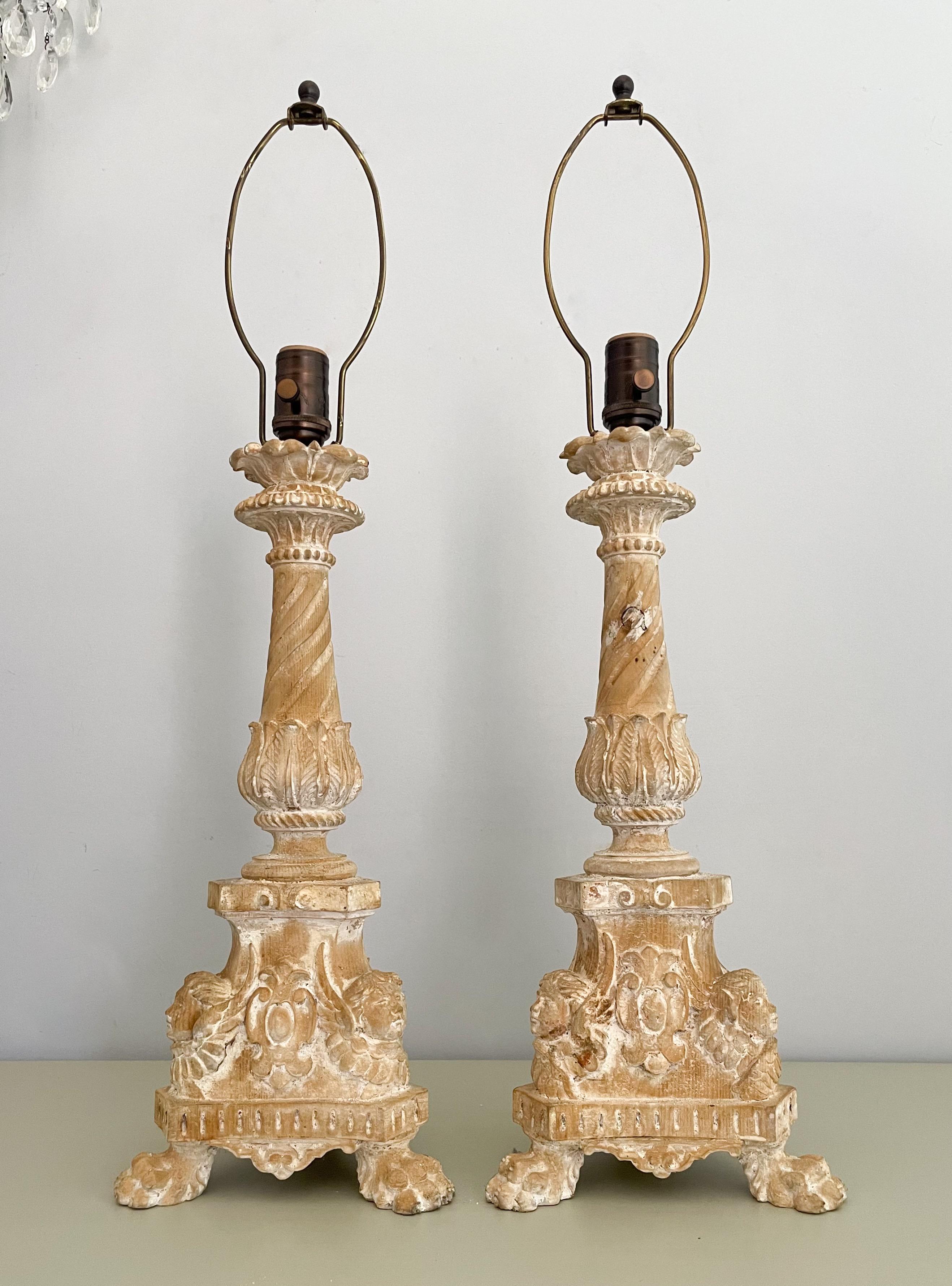 Beautiful, antique Italian carved wood candlestick lamps in the Baroque style.

Each lamp is made of solid wood with highly detailed carvings including a base with cherubs, crests and lion paw feet. 

Height of carved wood body is 18”

Small