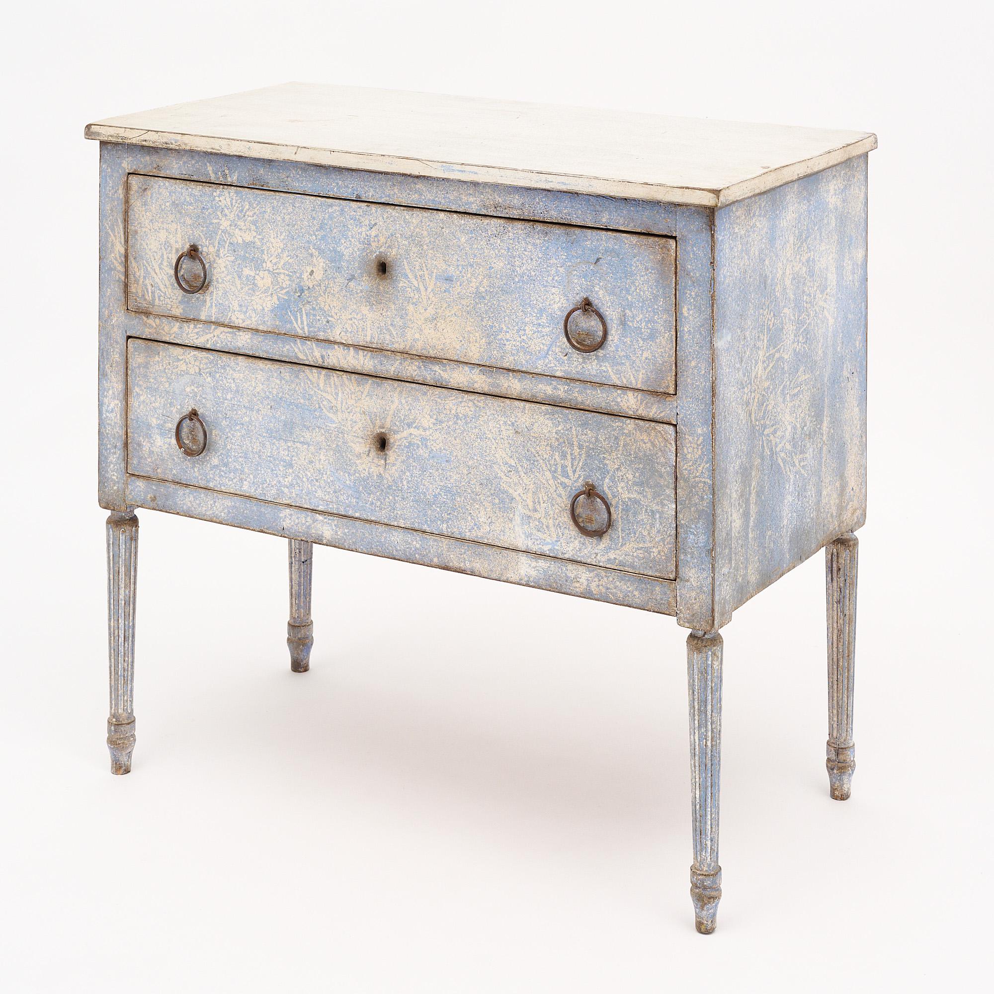 Italian chest with striking hand-painted design in cream and blue tones, supported by four fluted and tapered legs. The chest features two dovetailed drawers with original hardware. We love the delicate floral motif. This chest would be perfect for