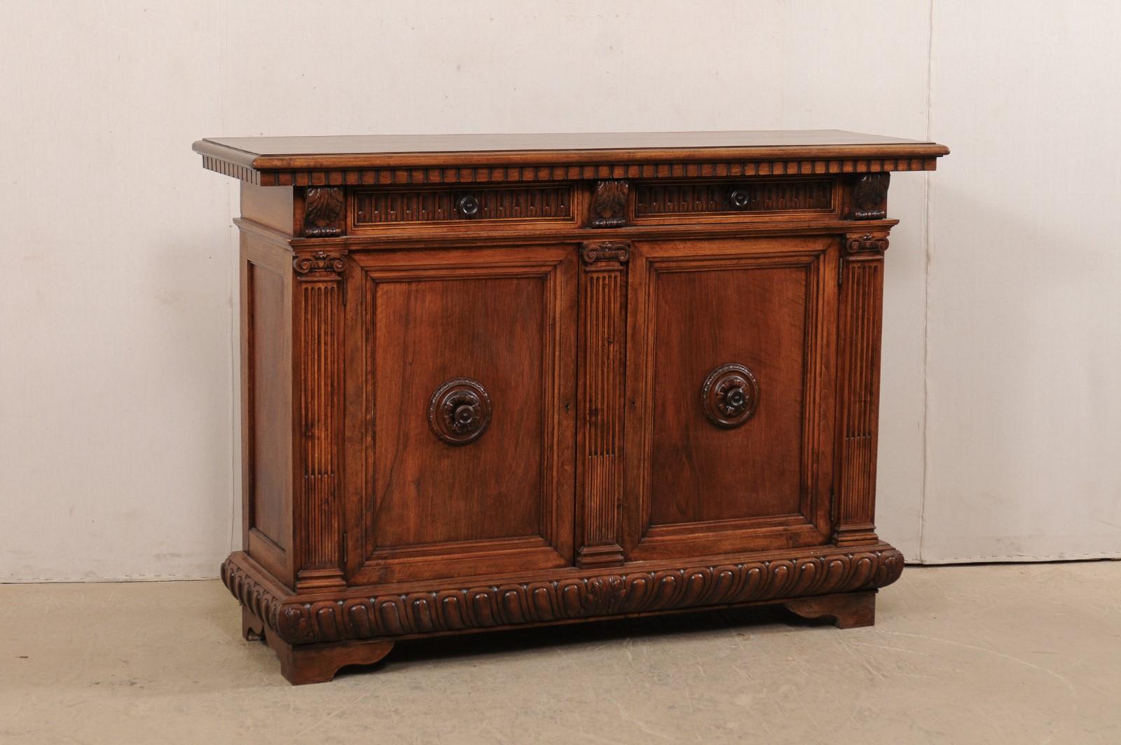 An Italian carved walnut wood credenza from the turn of the 19th and 20th century. This antique buffet from Italy features rich walnut wood which has been exquisitely carved with dentil trim, egg-n-dart trim, acanthus leaf accents, and fluted