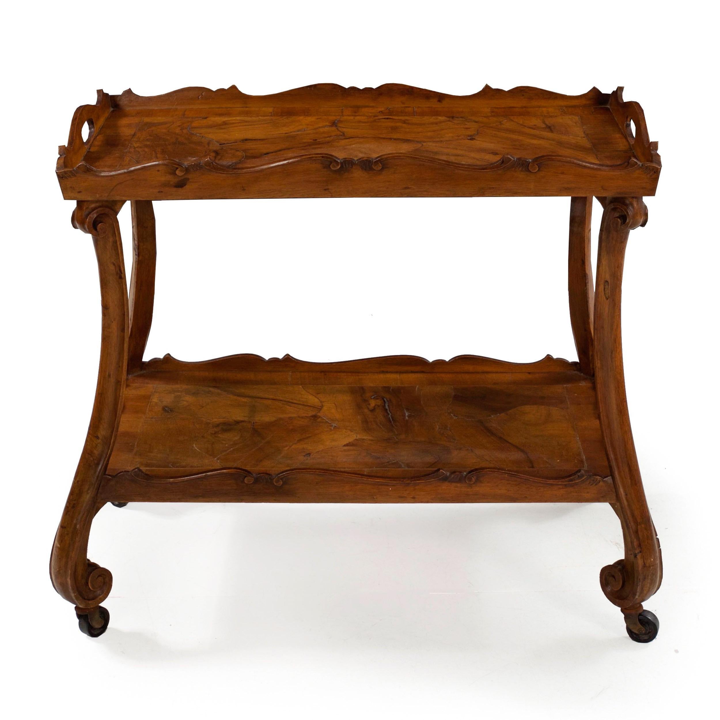 An attractive two-tier serving table designed with slices of unusually thick burl walnut veneers set in chaotic patterns against one another throughout either tray. This is framed in stringer inlays before a low scalloped rim with light incised