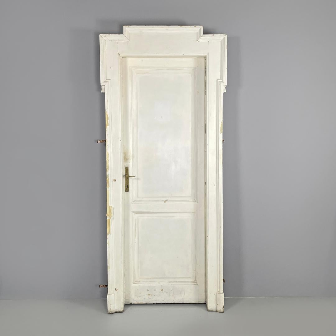 Puerta italiana antigua de madera pintada de blanco con marco y tiradores de latón de principios de 1900
Puerta con jamba de madera pintada de blanco. El marco exterior tiene líneas y decoraciones regulares y geométricas. Dentro del marco está la