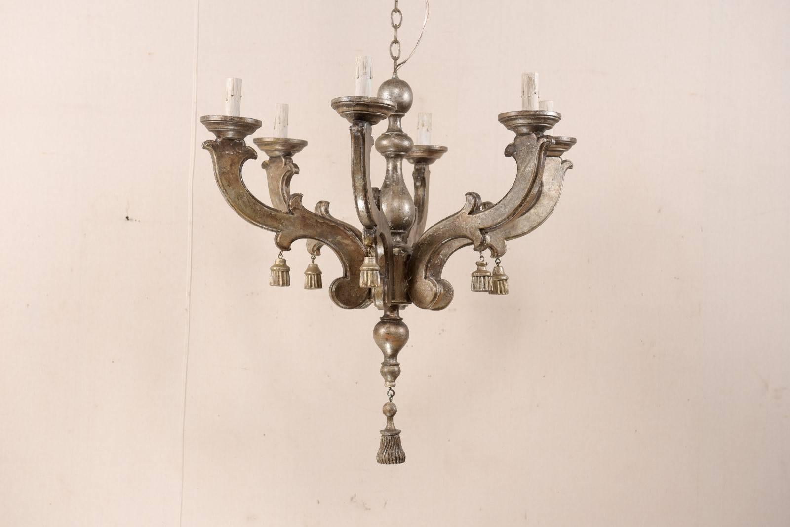 An Italian carved and painted wood chandelier from the mid-20th century. This exquisite Italian chandelier features a turned central column with six flat-sided carved foliage arms emerging from the center. Carved wood tassels hang about the