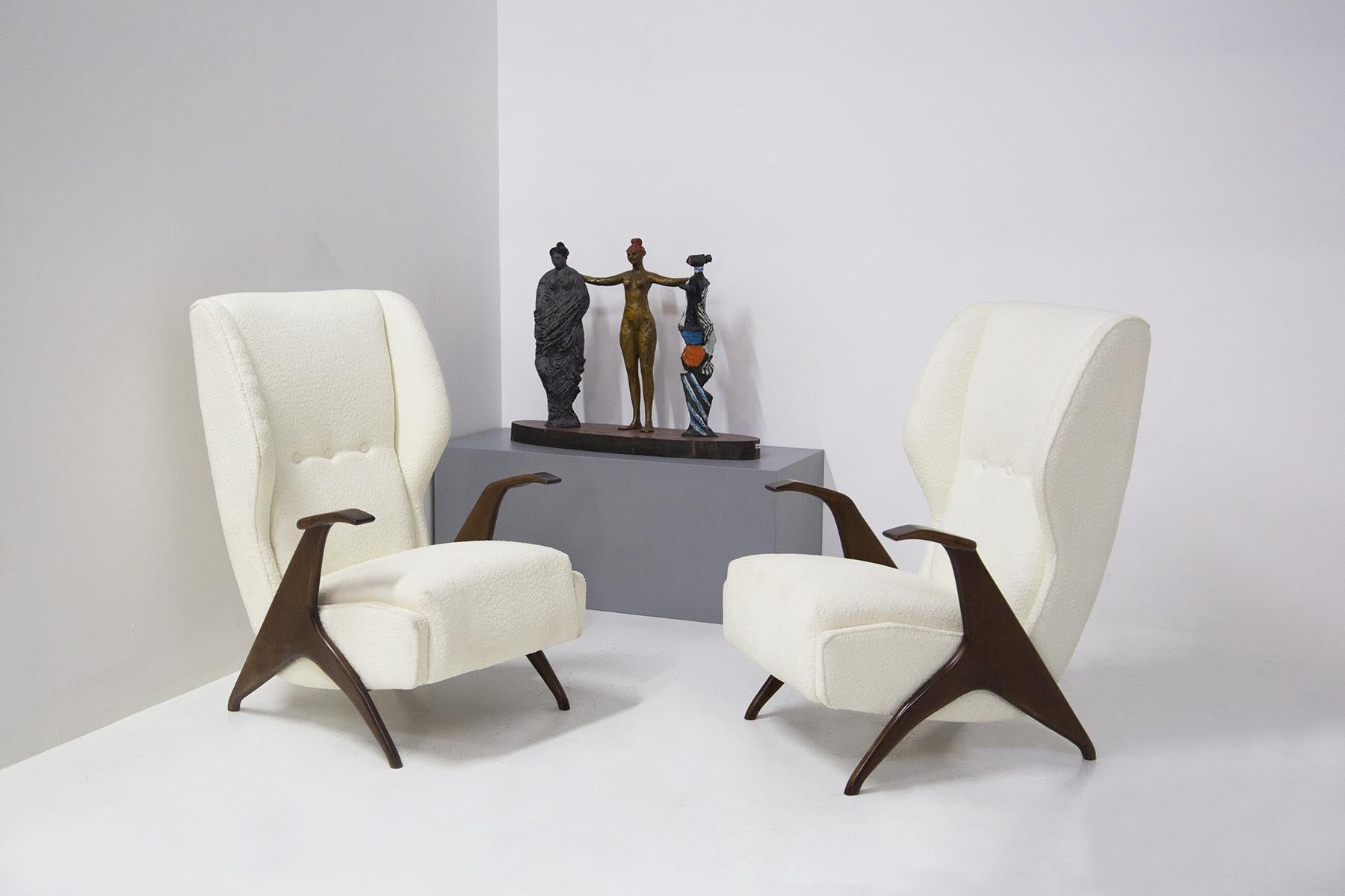 Elegant and comfortable pair of restored 1950's Italian armchairs. The pair of armchairs are upholstered in an elegant white bouclé fabric. While the frame, hand rests and feet are made of wood. The particularity of the armchairs are its two large