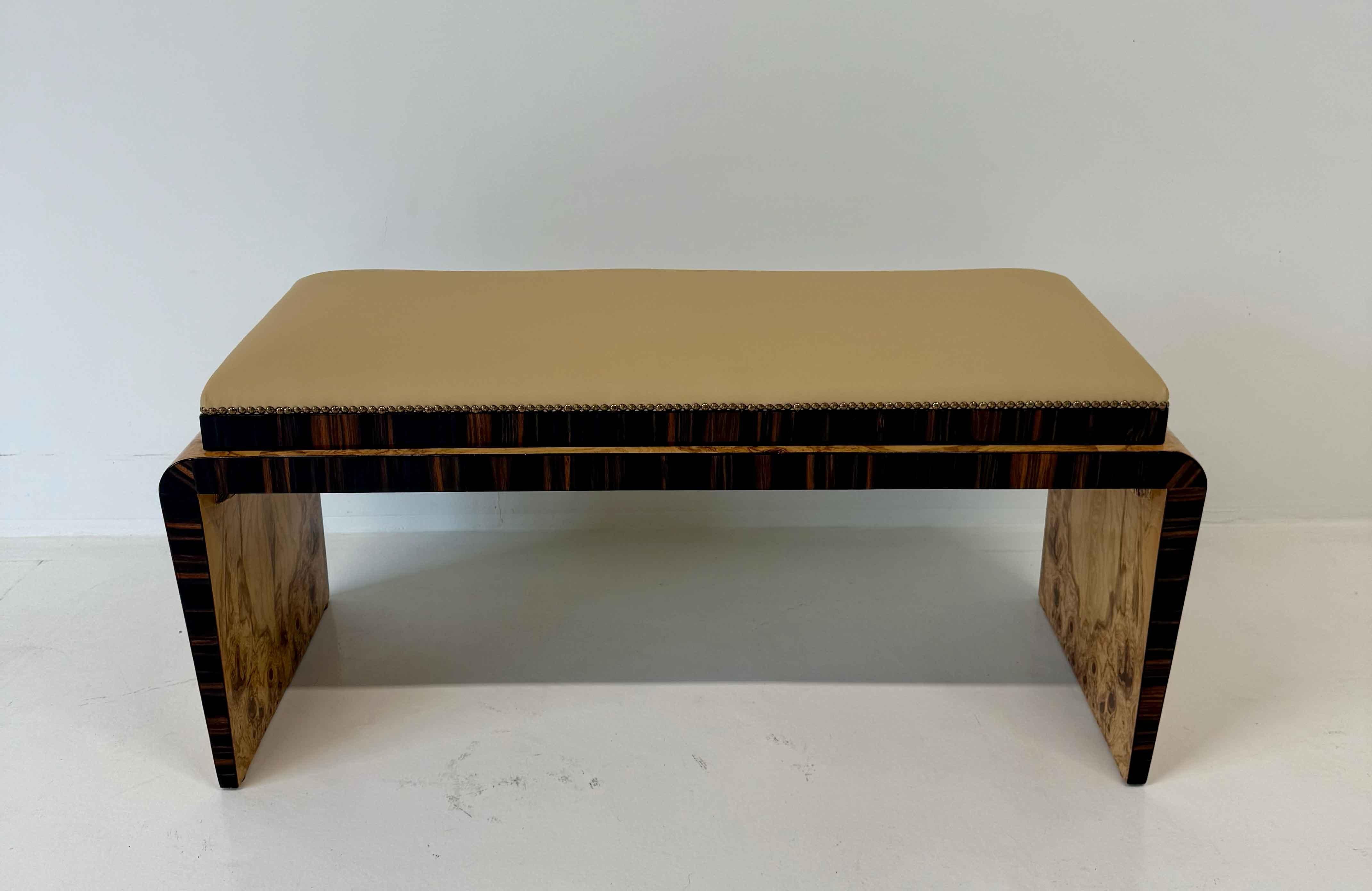 Elégante banquette italienne Art déco, années 1940.
La structure associe la loupe rare de frêne olivier au bois de Macassar, créant un contraste saisissant de tons et de textures. L'assise est recouverte d'un similicuir raffiné qui assure à la fois