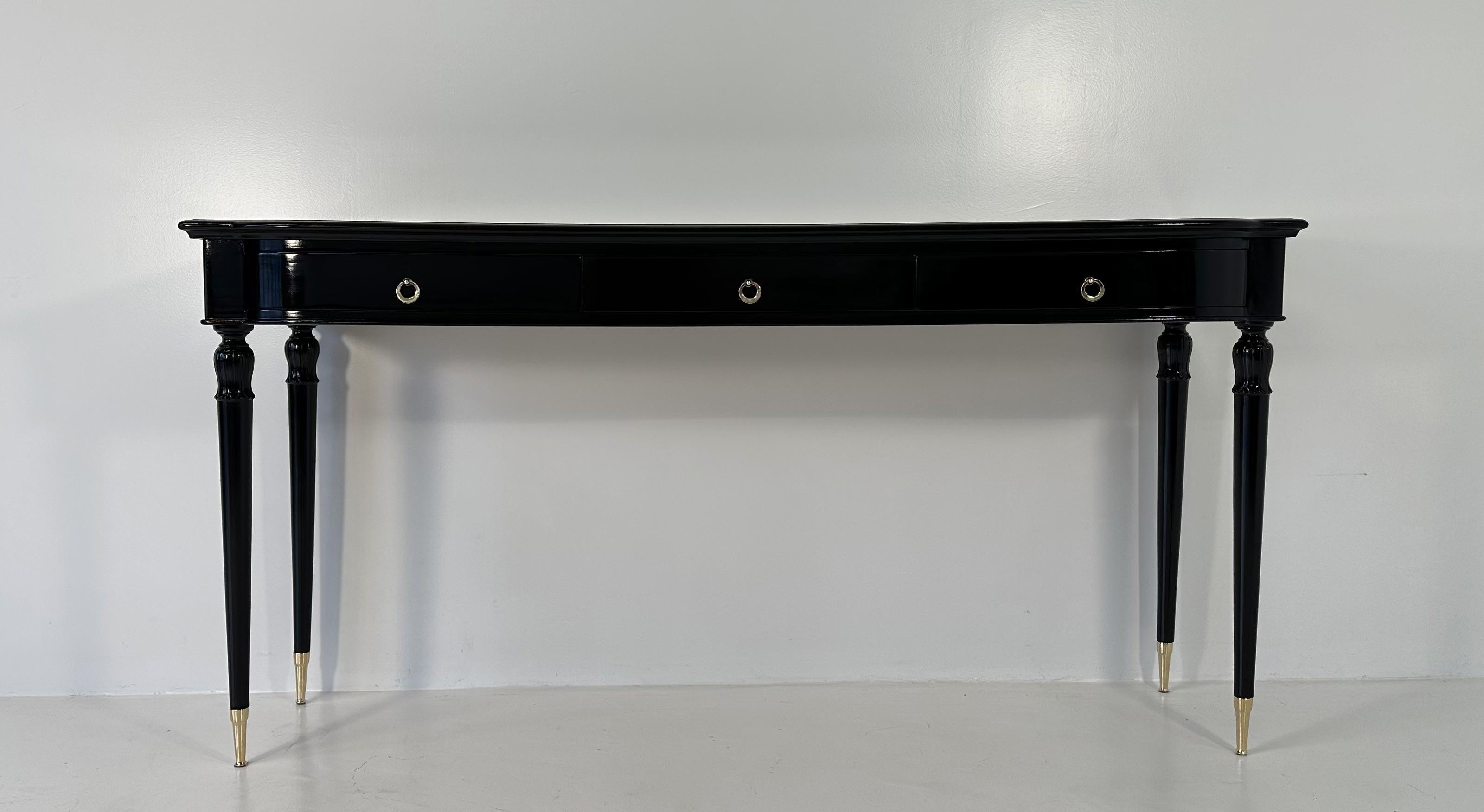 This stunning Art Deco Console Table was produced in Italy in the 1950s and it reminds the style of Paolo Buffa. 
It is completely black lacquered and has a black glass top. The tips, the handles, the keys and the keyholes are in brass. 
The