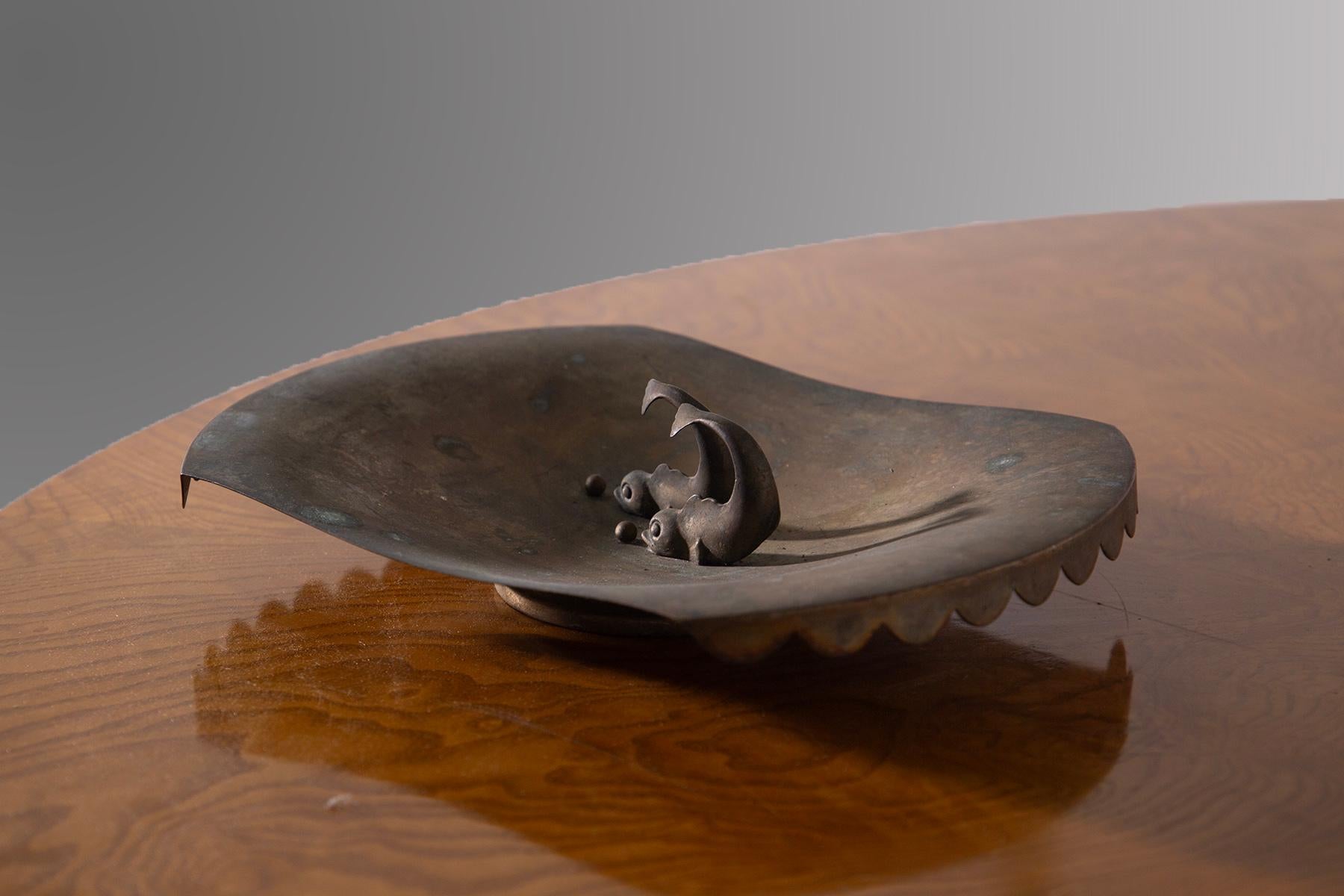 Este encantador centro de mesa Art Déco italiano, de latón y de los años 20, es un objeto decorativo de gran valor y elegancia. La forma rectangular con esquinas redondeadas se enriquece con un borde ondulado que recorre todo el contorno, dando un